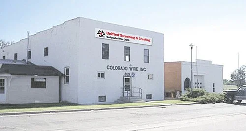 White commercial building with signs for Colorado Wire Inc. and Unified Screening & Crushing with a clear sky in the background.