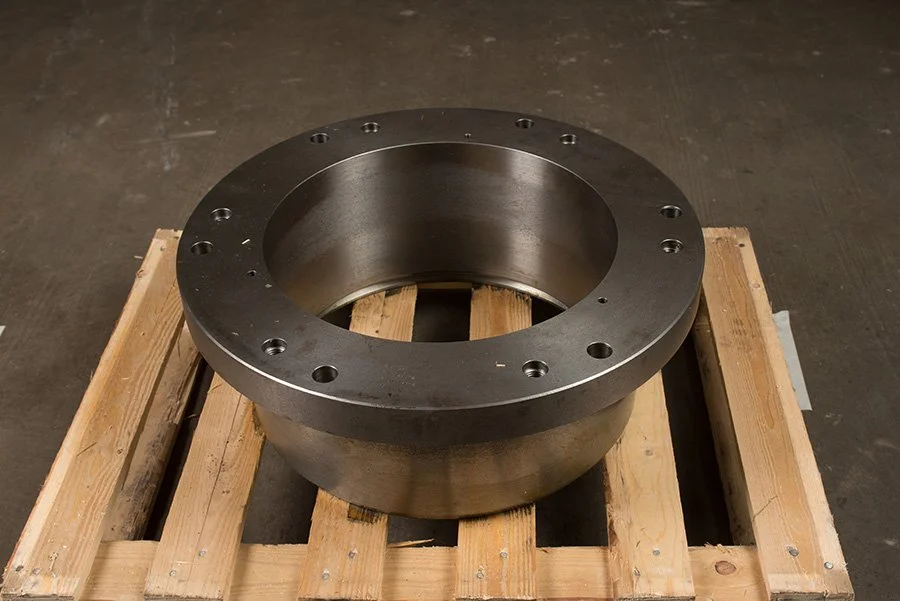 Metal ring component with bolt holes resting on a wooden pallet in a workshop or warehouse.