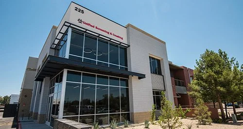 Exterior view of a modern commercial building with large glass windows, signage indicating it is United Healthcare & Community, and a blue sky background.