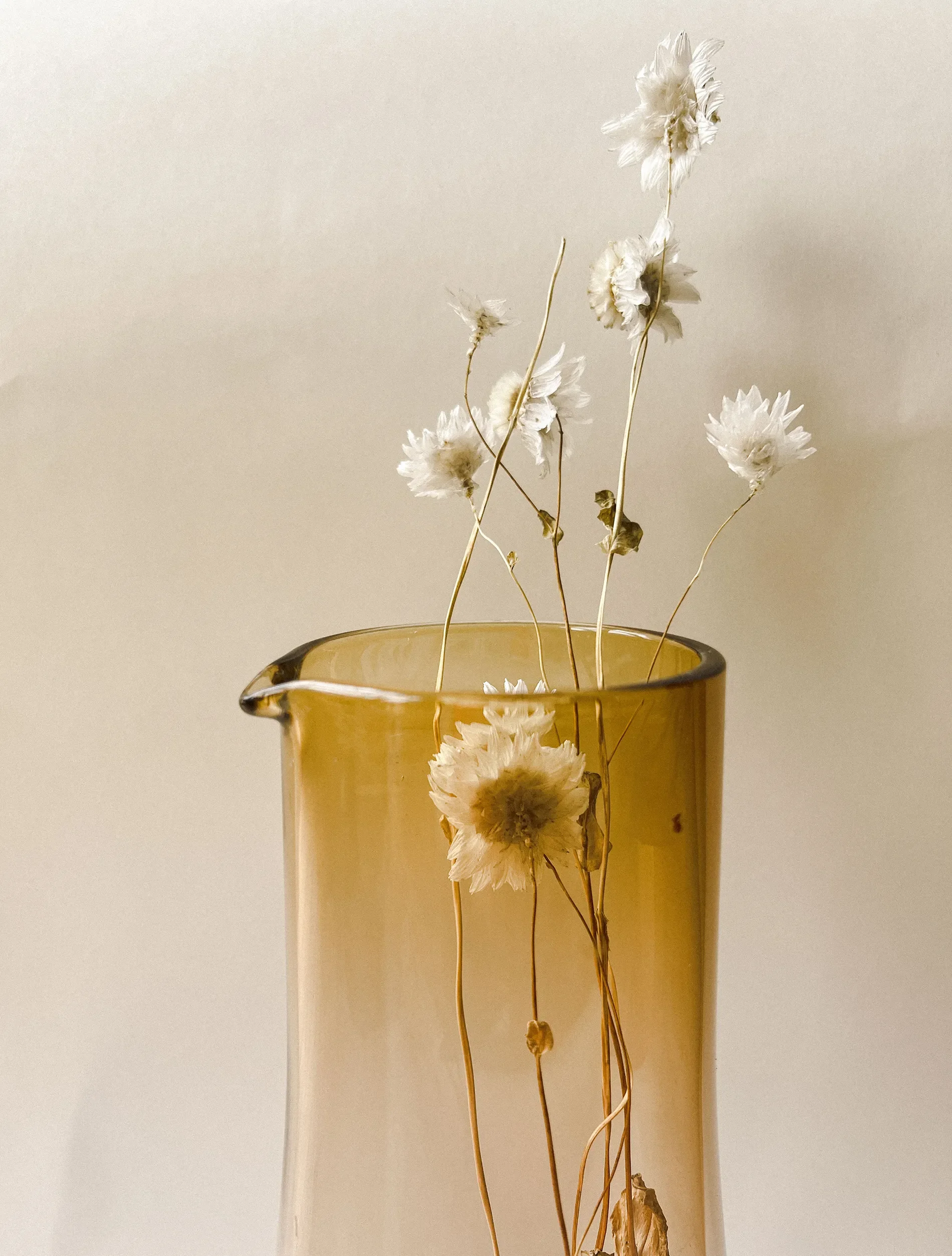 Dry white flowers in a yellow glass vase against a plain, light-colored background.