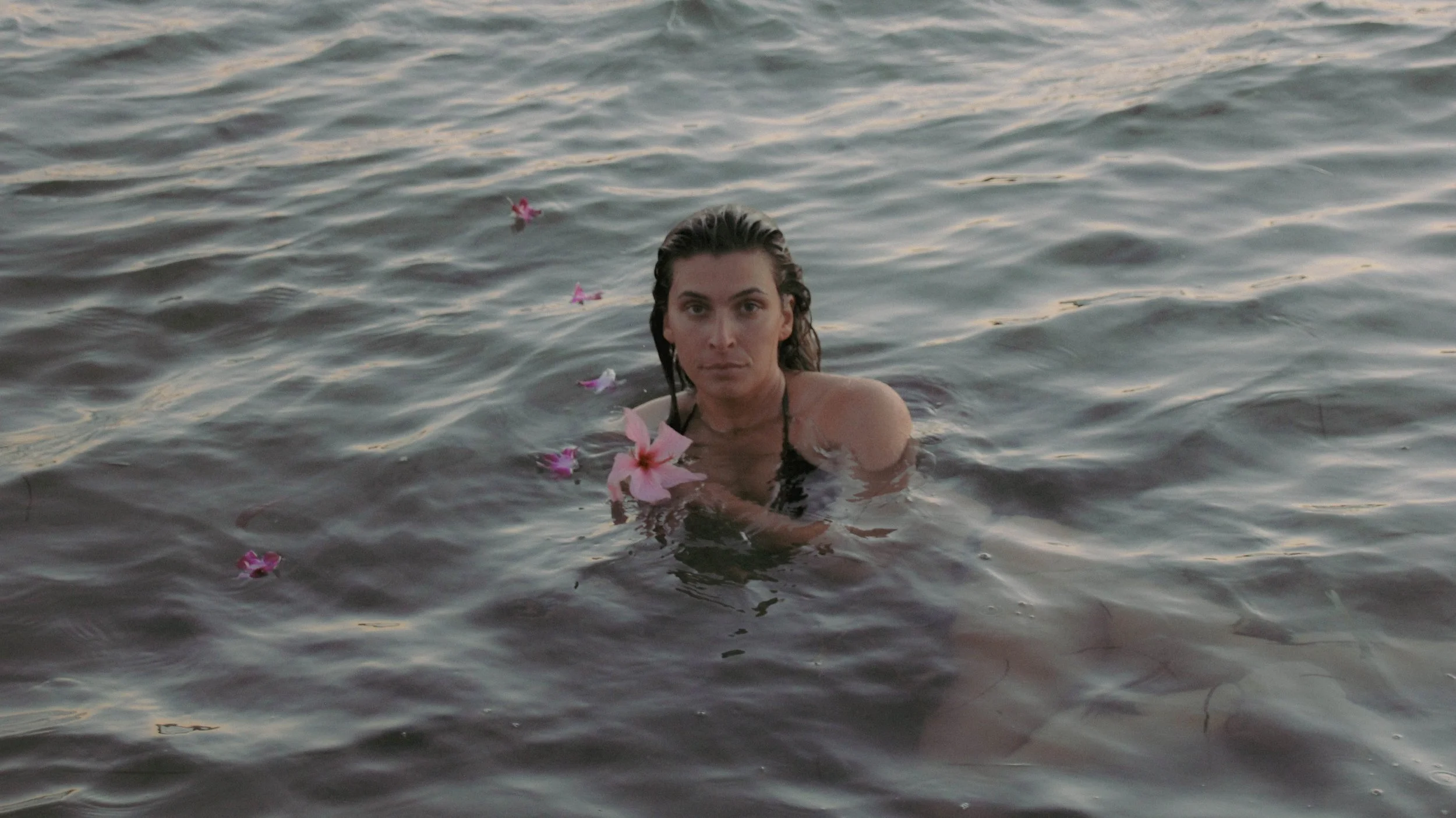 A woman with wet hair in the water, surrounded by pink flowers floating on the surface.