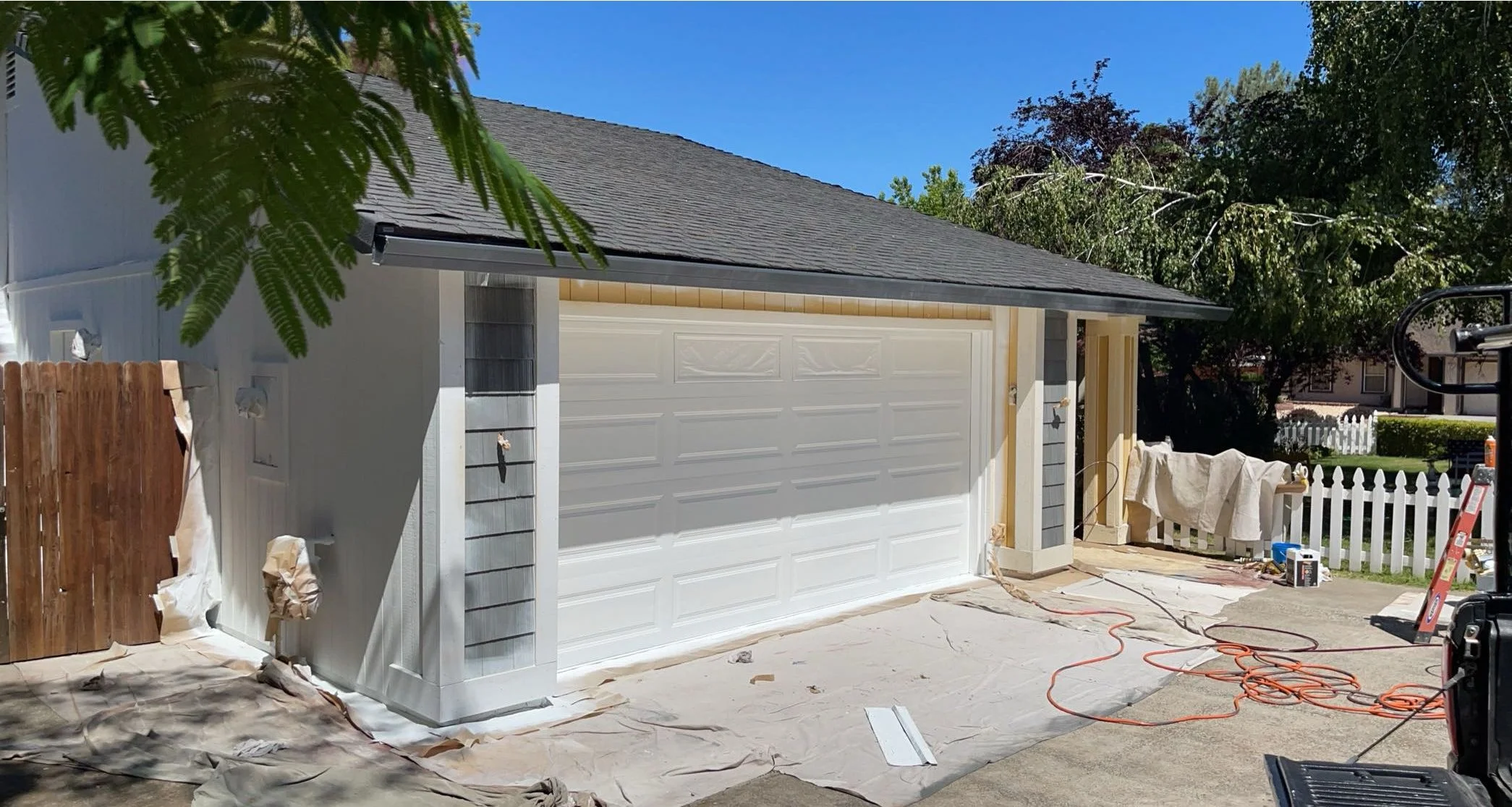 Professional exterior house painting in progress on a residential home with fresh paint being applied to the siding and garage door.