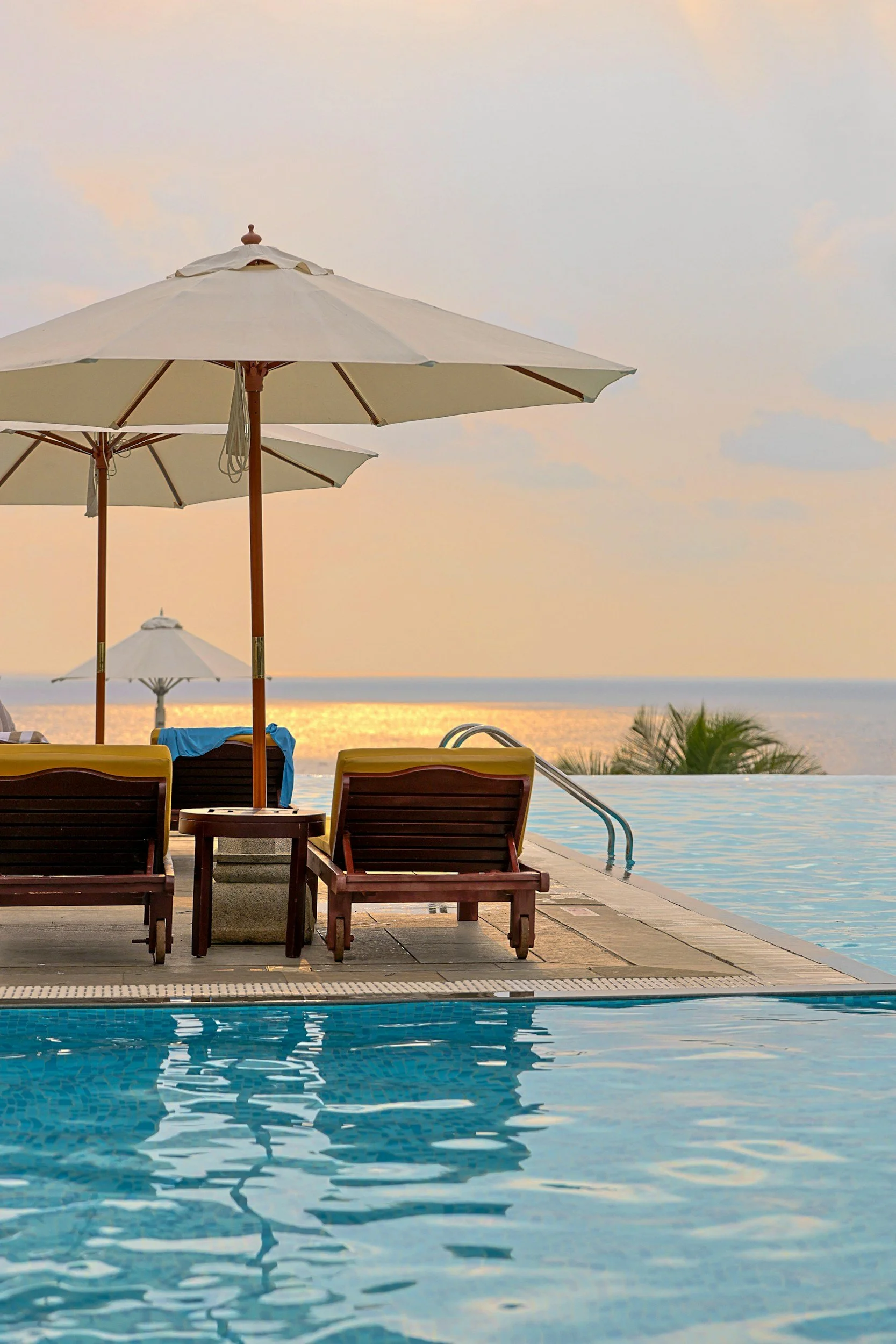 A poolside scene with lounge chairs, umbrellas, and a view of the ocean at sunset.