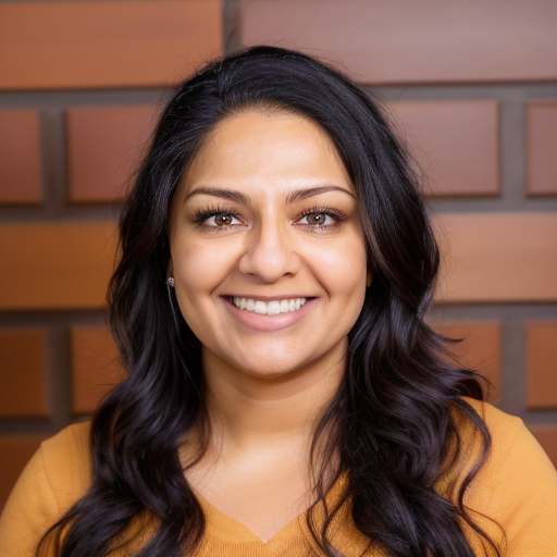 Portrait of a woman with dark wavy hair smiling against a brick wall background.