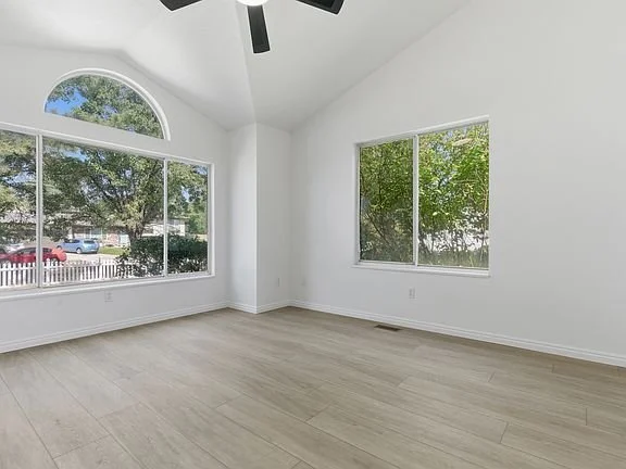 Empty room with large windows, white walls, and light-colored flooring.