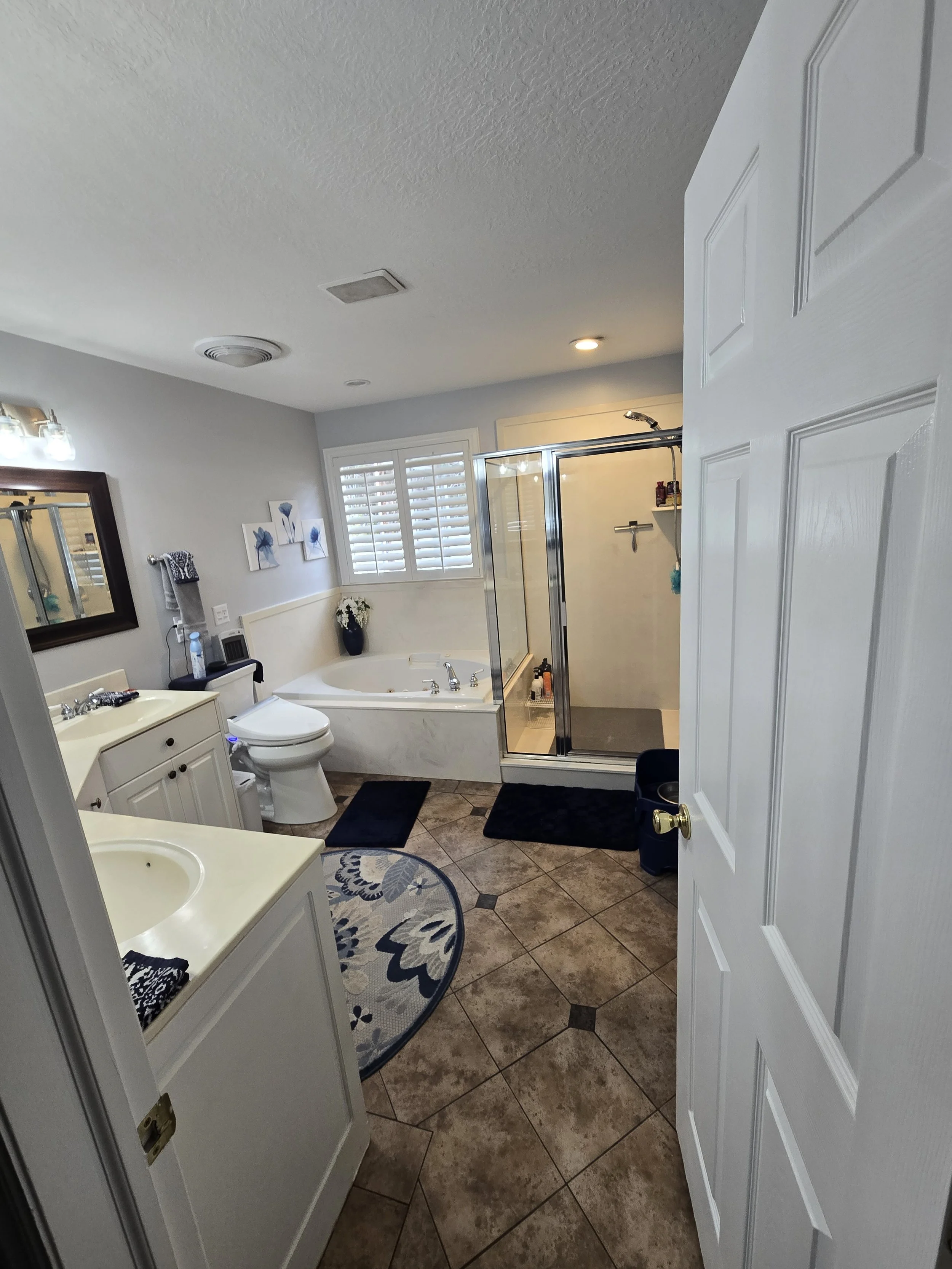 A bathroom featuring a shower with glass door, a bathtub, a toilet, a vanity with sink, and decorative elements like a mirror, artwork, and a vase with flowers.