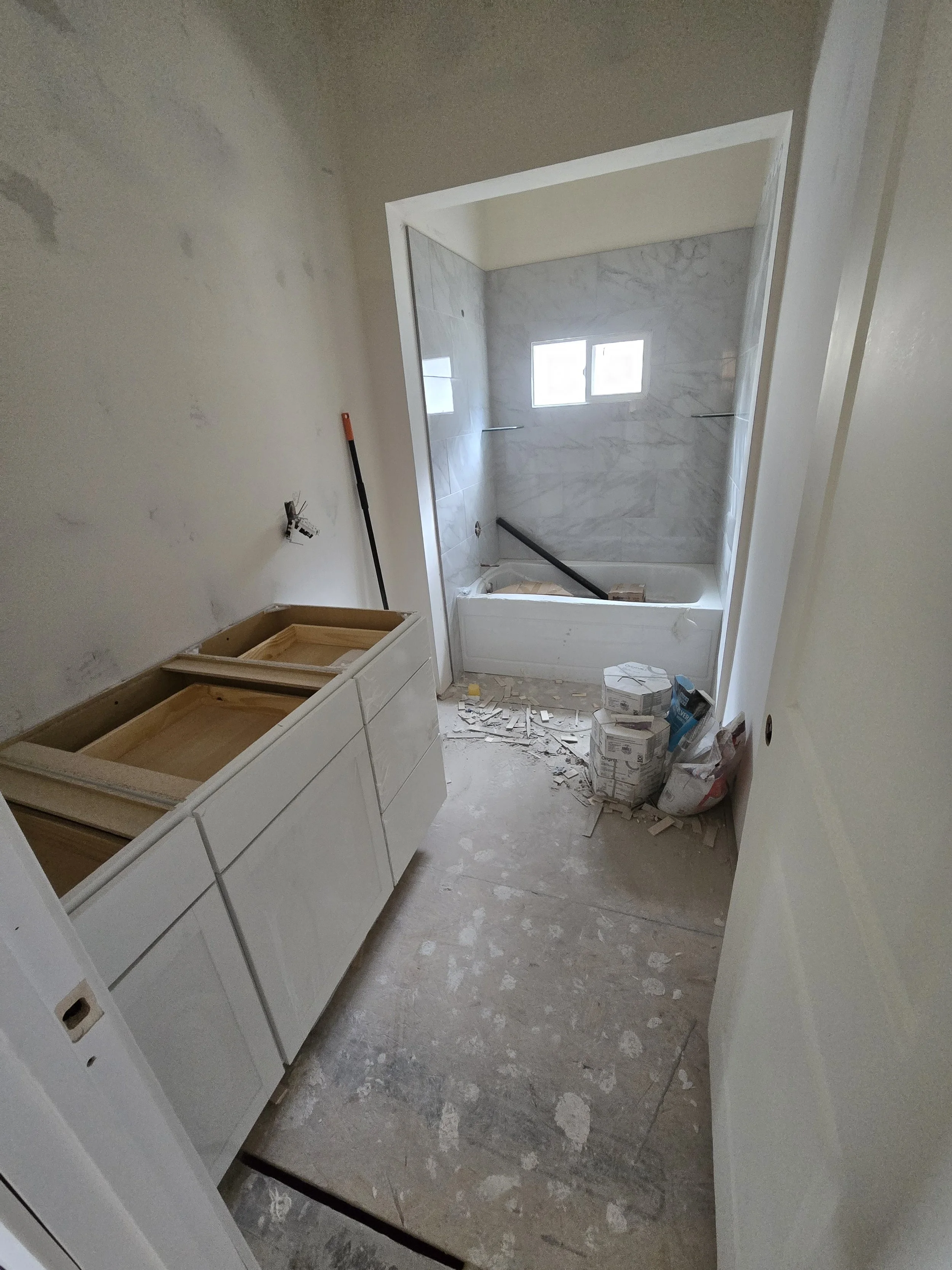 Renovation site with white cabinets on a bathroom or kitchen wall, construction materials, and debris on the floor.