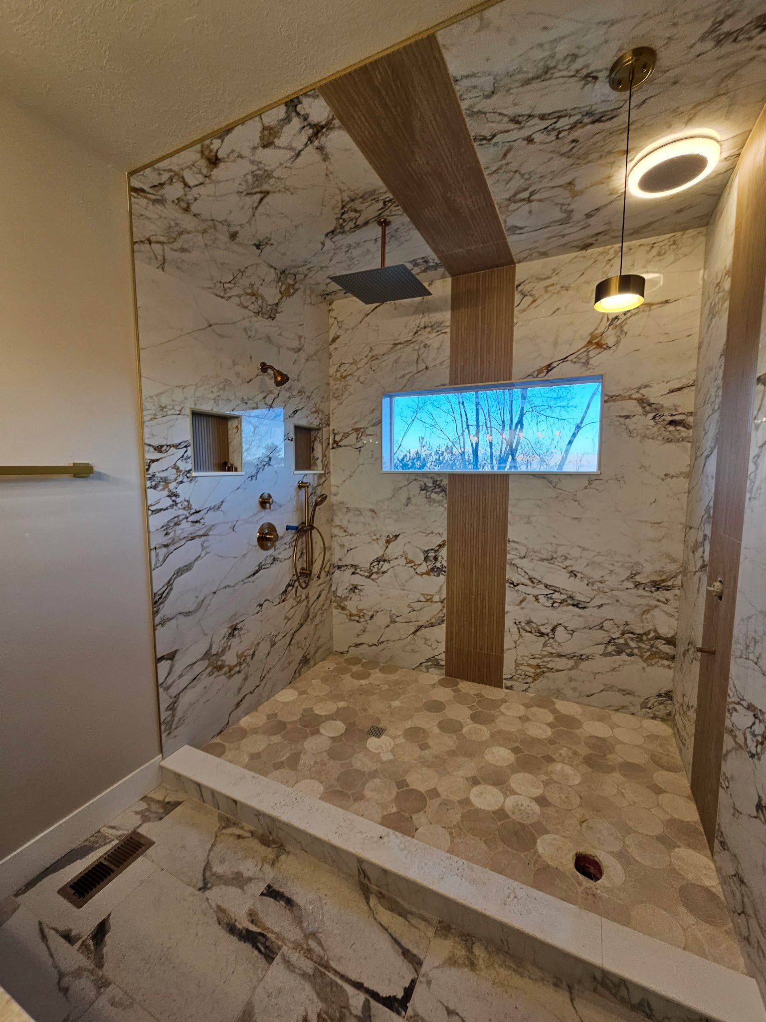 Modern bathroom with marble walls, a rain showerhead, and a small window showing a tree outside.