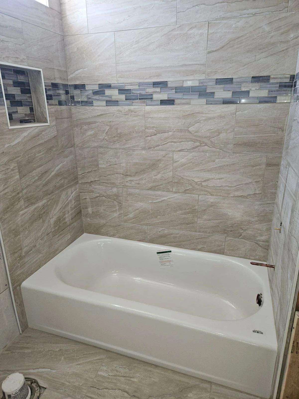 Bathroom shower with beige and blue tile walls and a white bathtub.