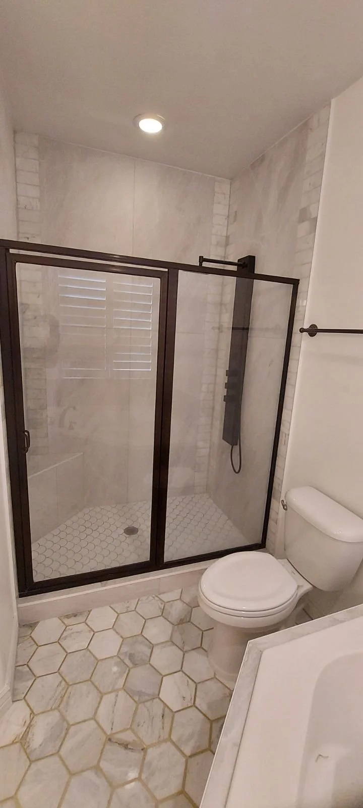 Bathroom with a glass-enclosed shower, toilet, and hexagonal marble floor tiles.