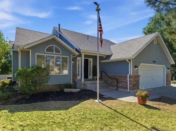 Blue house with gray roof, front porch, solar panels, flagpole with American flag, and a potted plant outside.
