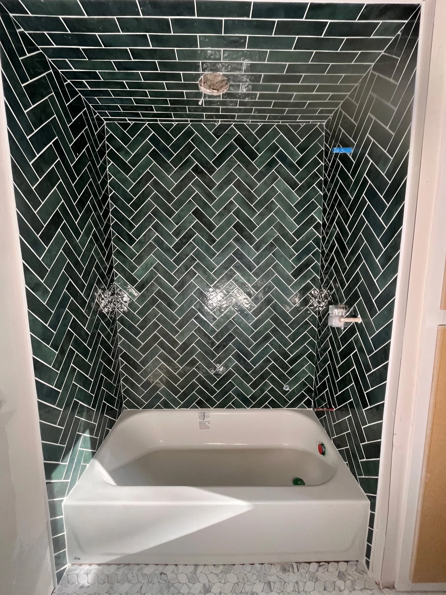 A bathroom with black subway tile walls arranged in a herringbone pattern, a white bathtub, and a partial view of the adjacent beige wall and wooden cabinetry.