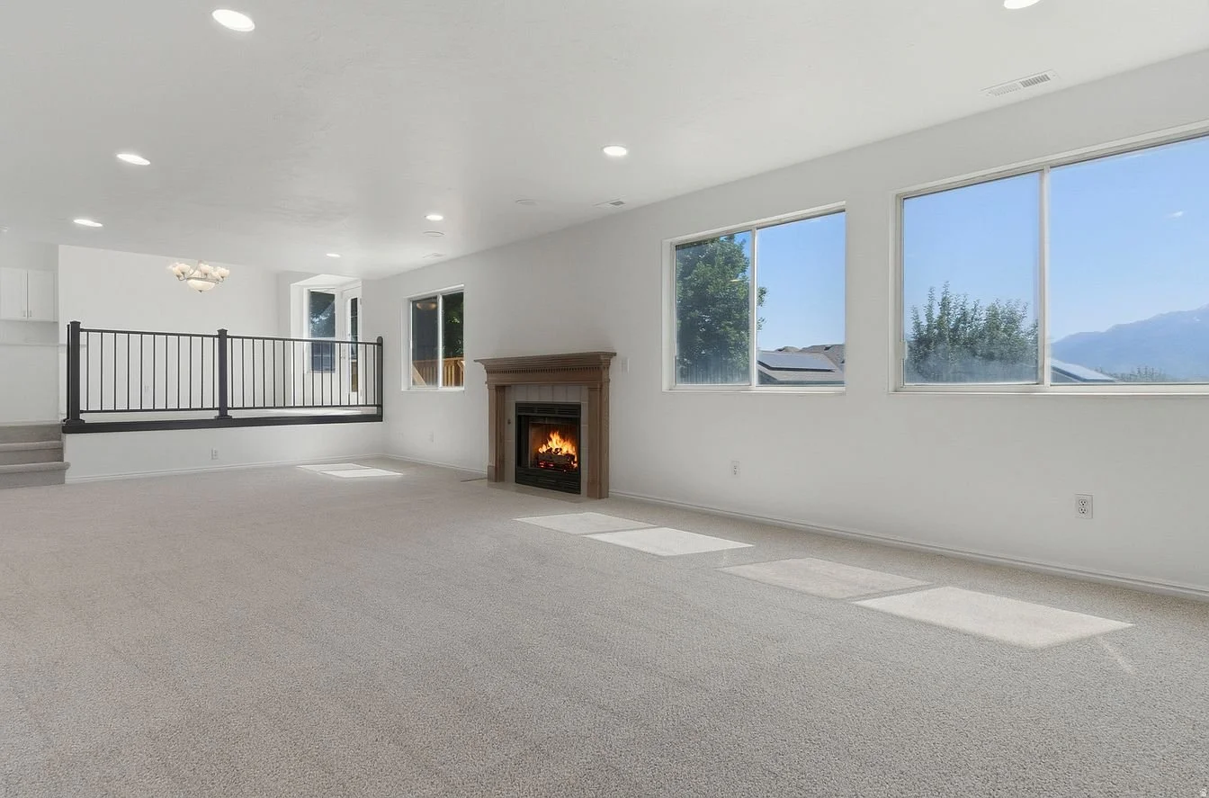 Empty living room with fireplace, large windows showing a view of mountains, and carpeted floor.