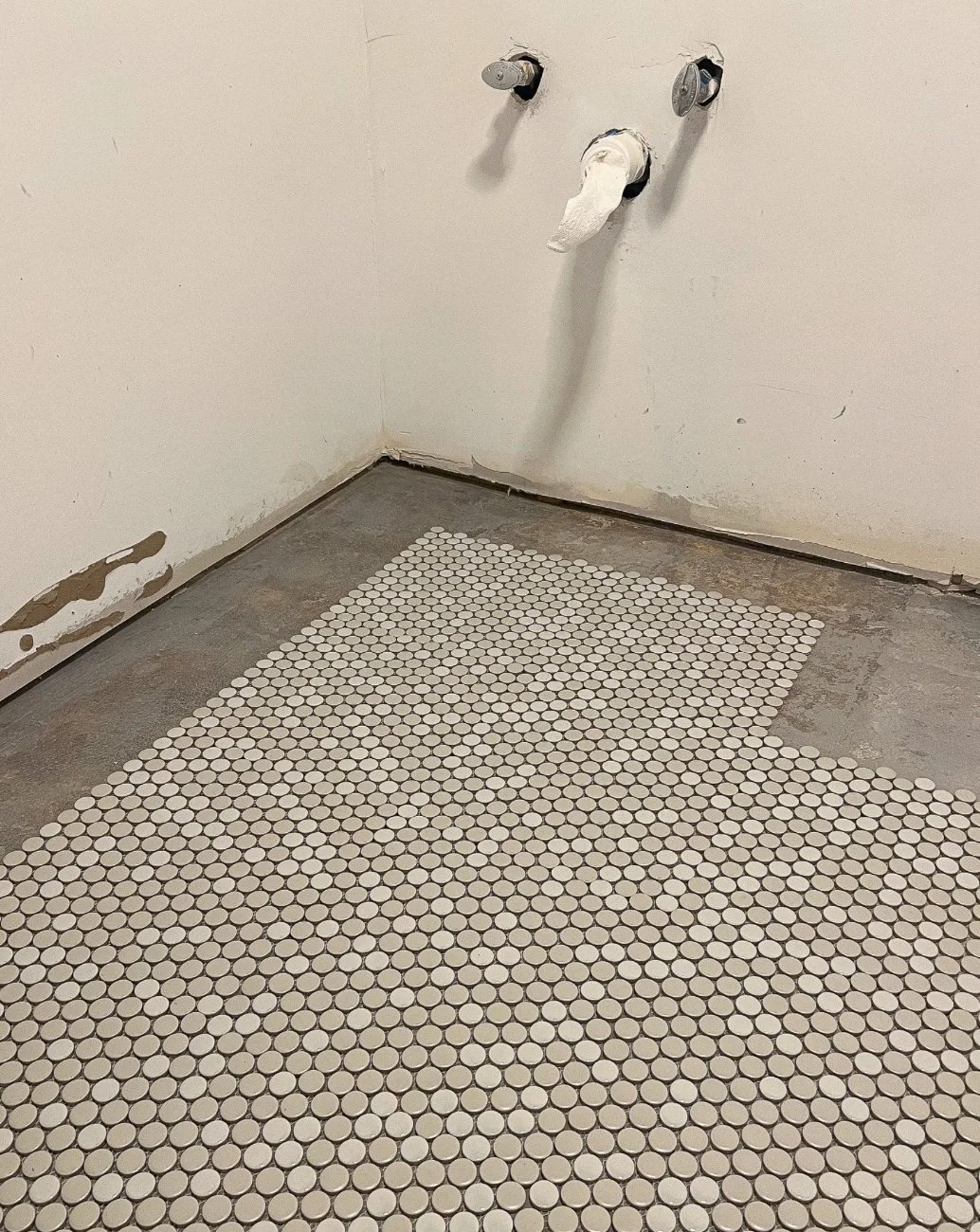 Empty bathroom with exposed plumbing pipes on the wall and white small tile flooring.