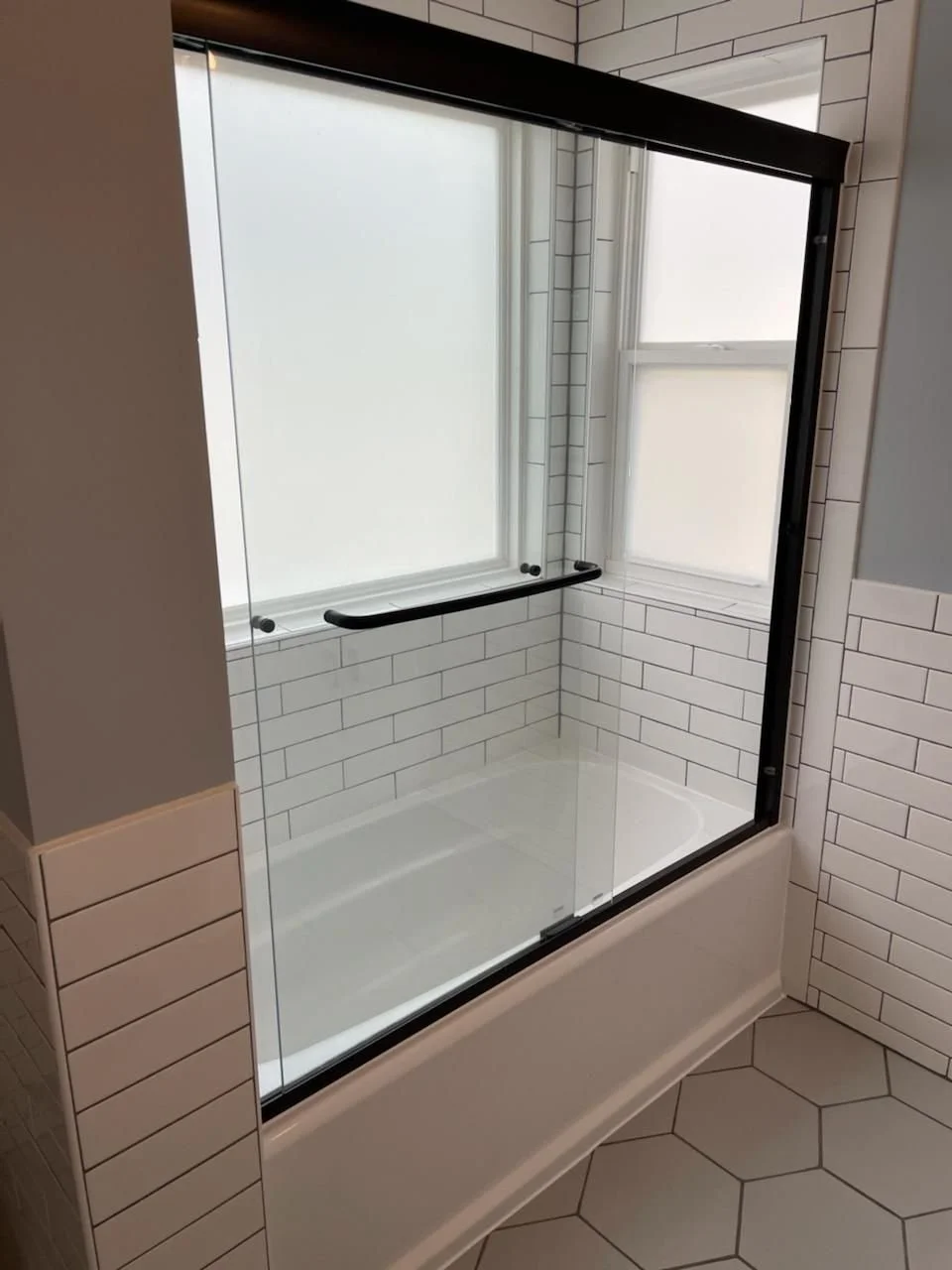 Bathroom shower with glass enclosure, white subway tiles, and a window with frosted glass