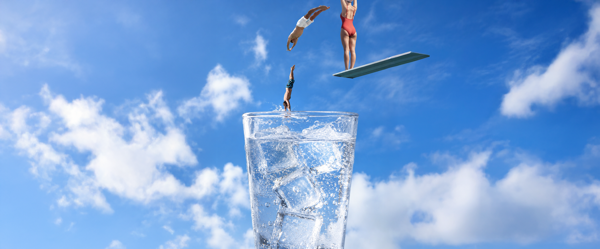 Miniature gymnasts performing synchronized flips into a tall glass of ice water against a blue sky with clouds.