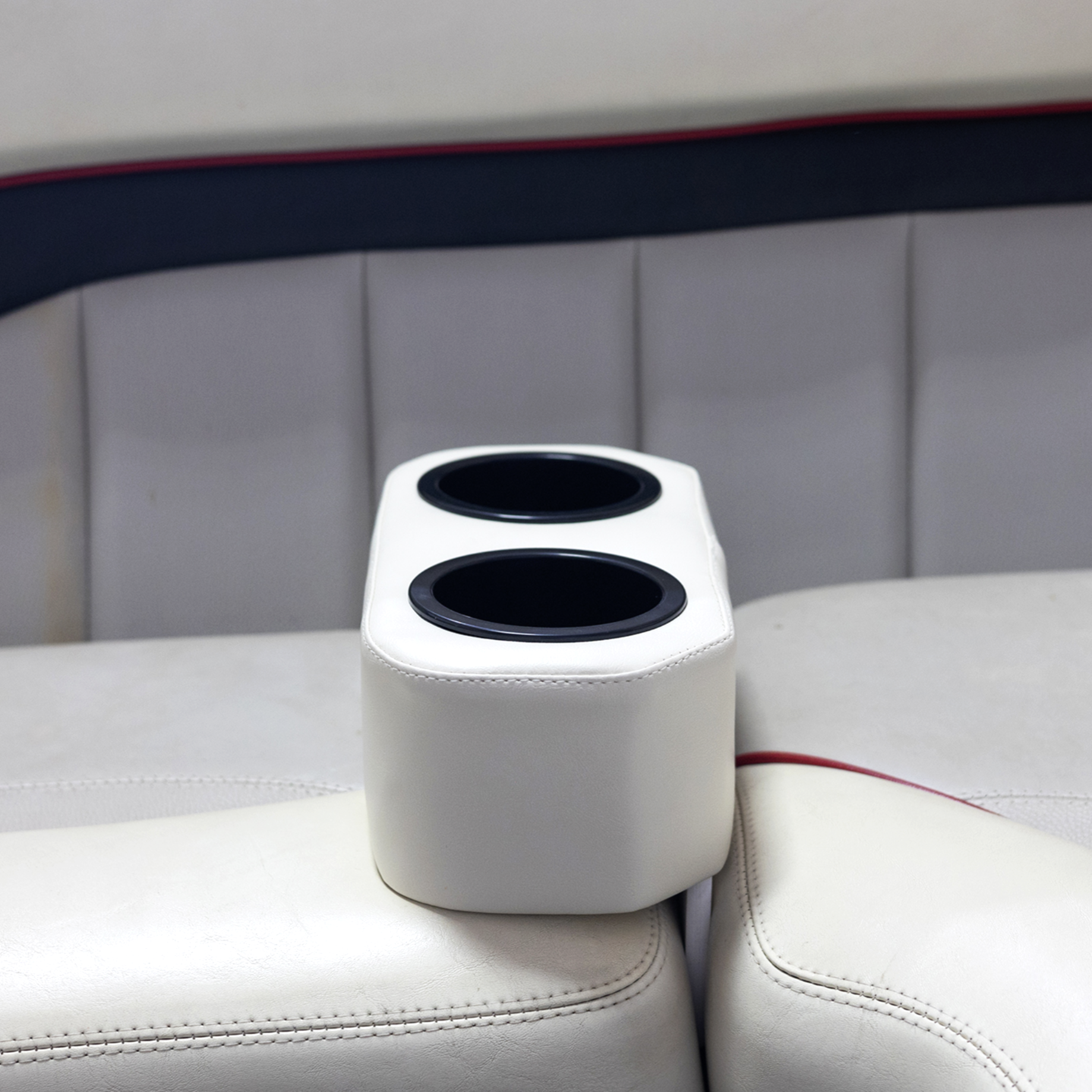 Close-up of a white speaker with two black speaker holes, placed on a white padded surface in front of a black and gray headboard with padded upholstery and red trim.