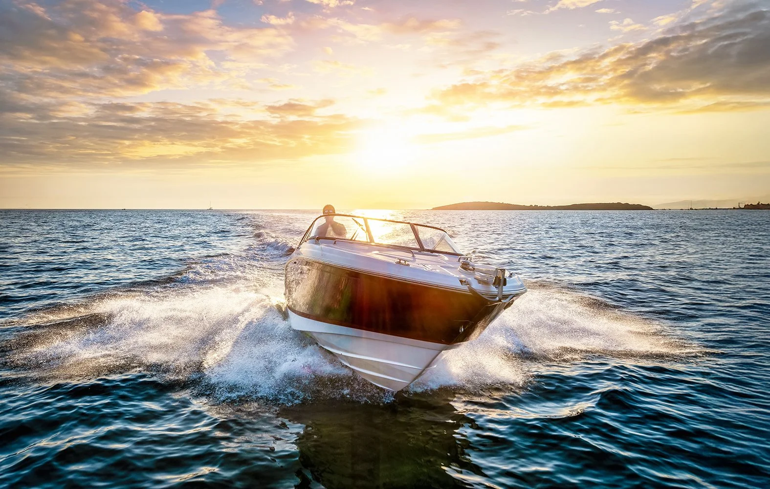 A boat speeding across the water during sunset with a bright sky and distant shoreline.