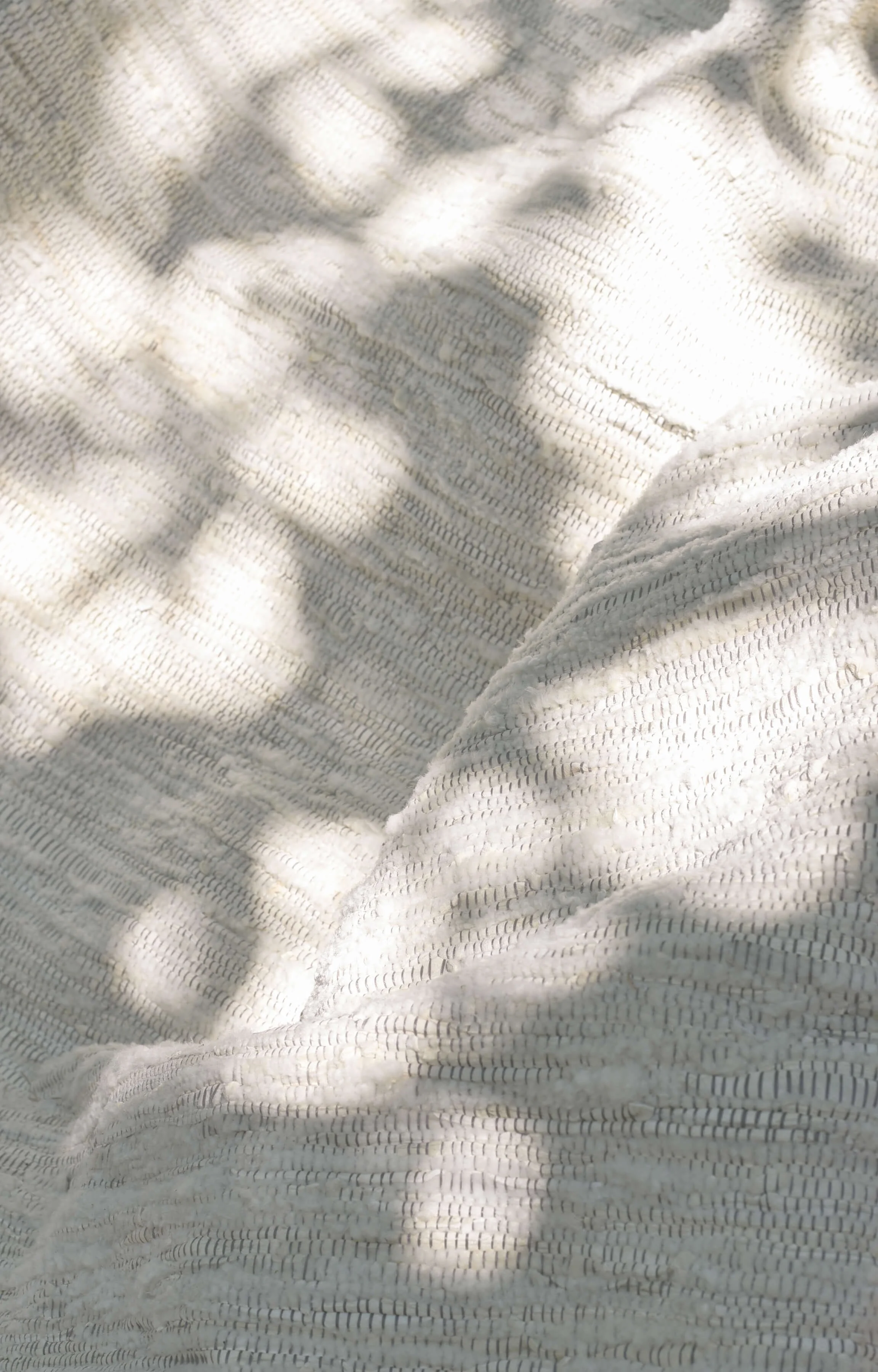 Close-up photograph of a textured white fabric with shadows cast on it.