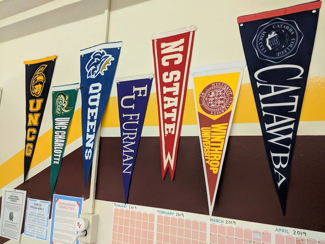 College pennants hanging on a wall, representing various universities including UNC G, UNC Charlotte, UNC Greensboro, Fayetteville State University, Winston-Salem State University, and Catawba College.