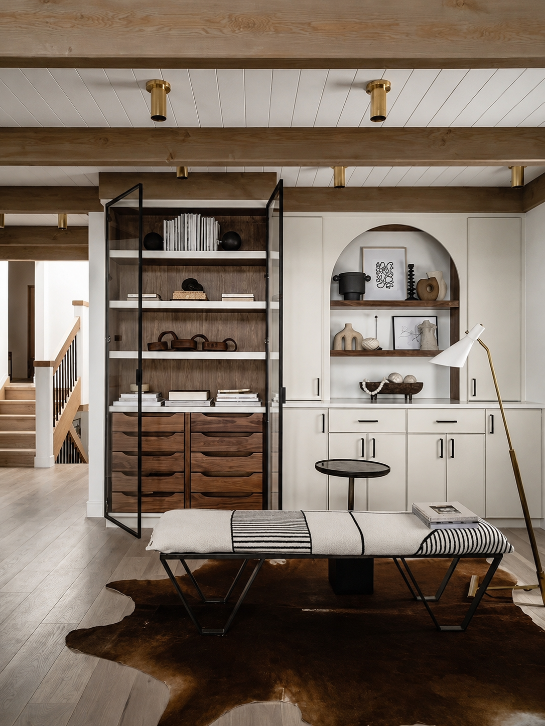Living room with wood accents, built-in shelves with decor items, a white bench with black and white fabric, and a cowhide rug.
