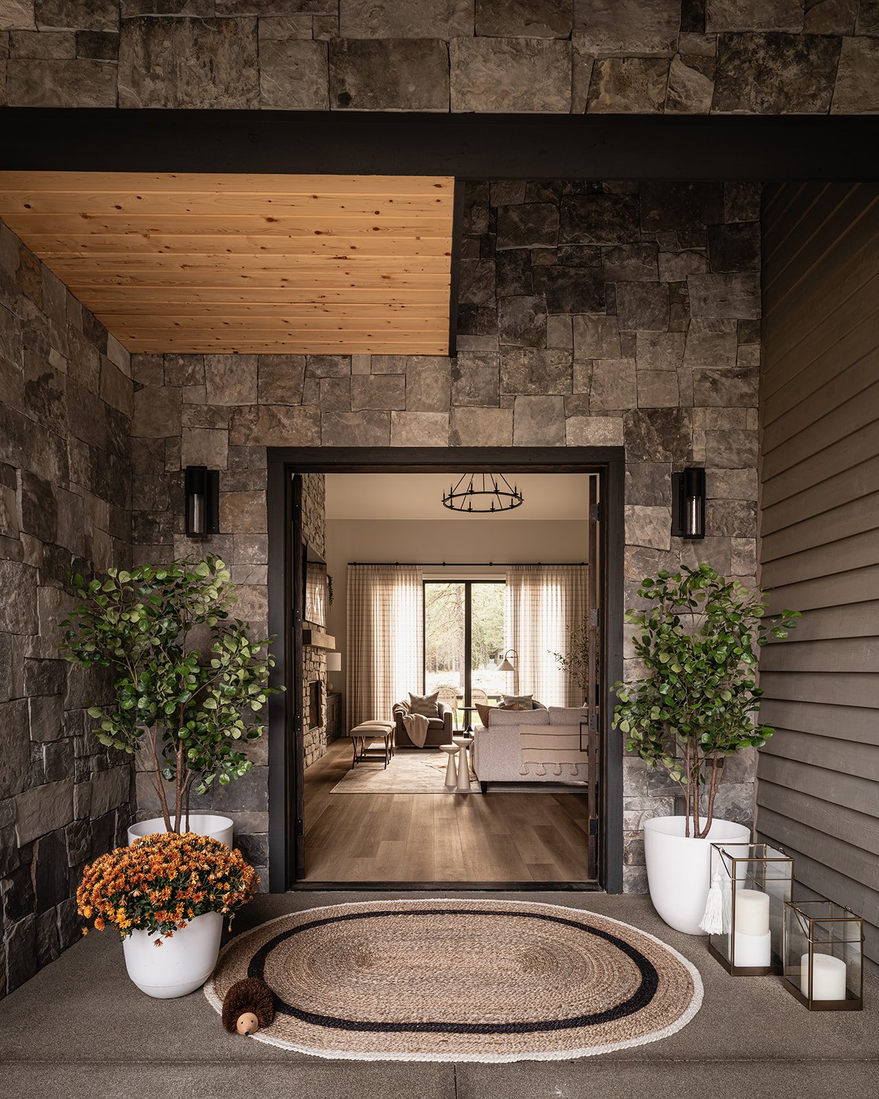 Entryway with stone walls, potted plants, a circular rug, and a view into a living room with sofas, curtains, and a sliding glass door.