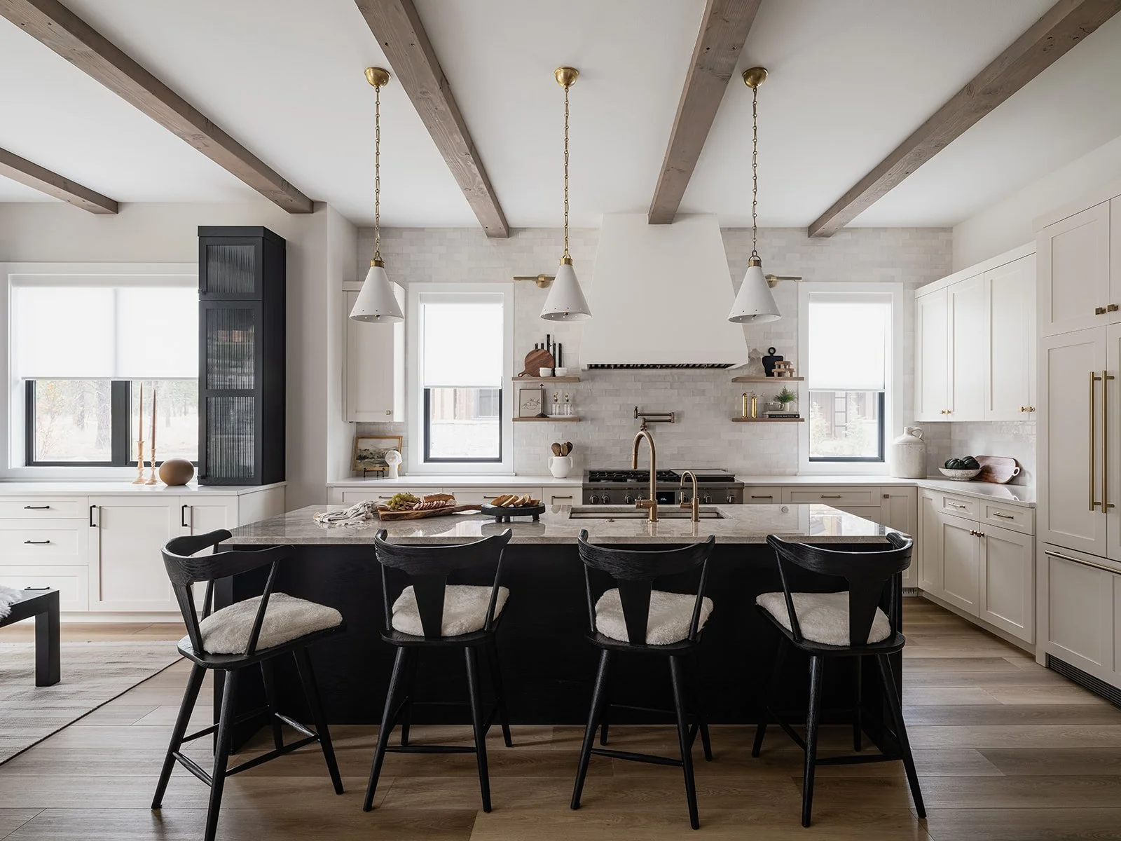 Modern kitchen with white cabinets, black chairs, and a large island with a granite countertop, pendant lights, and windows with white blinds.