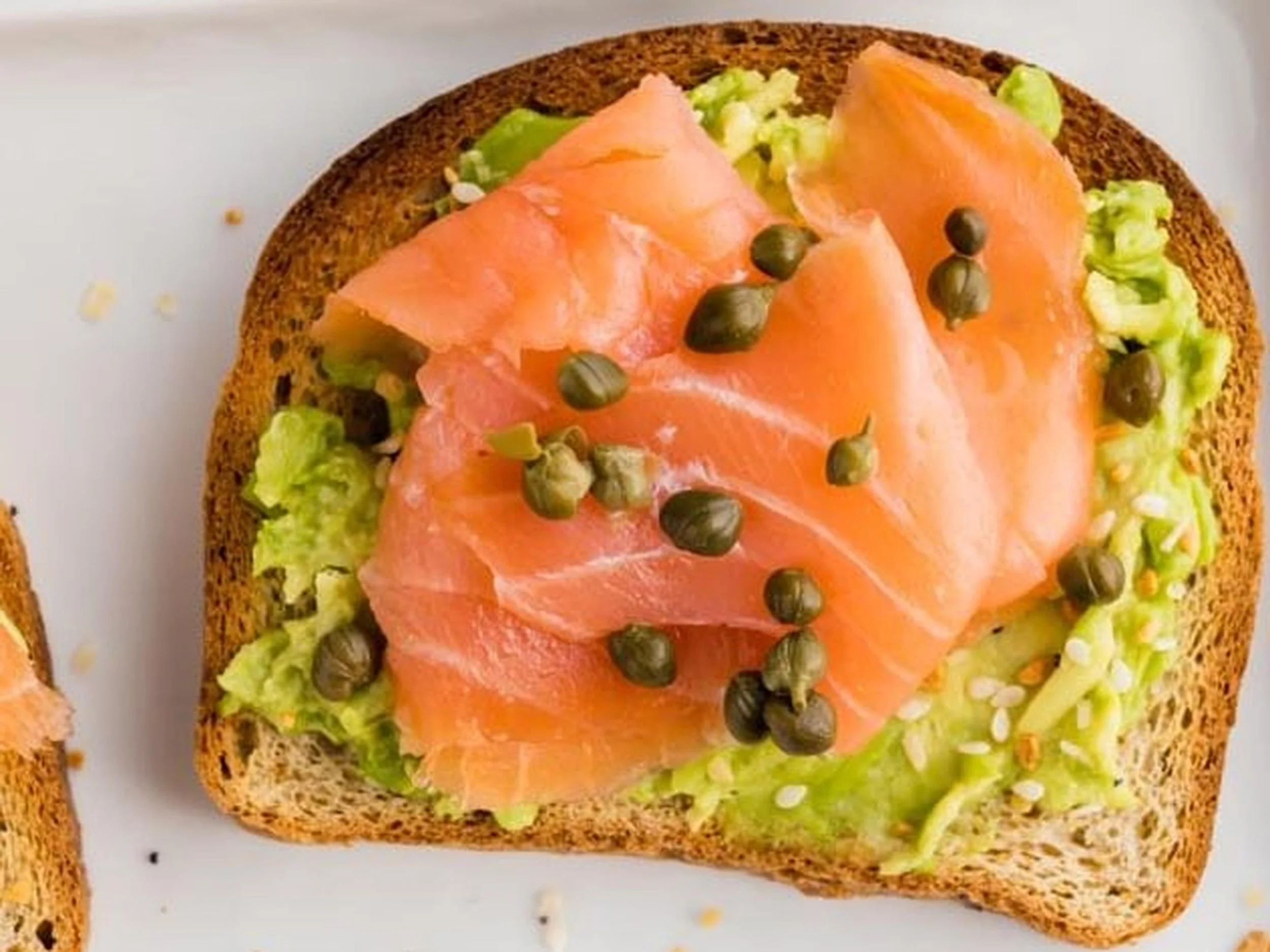 A slice of toasted bread topped with smoked salmon, avocado, and capers.