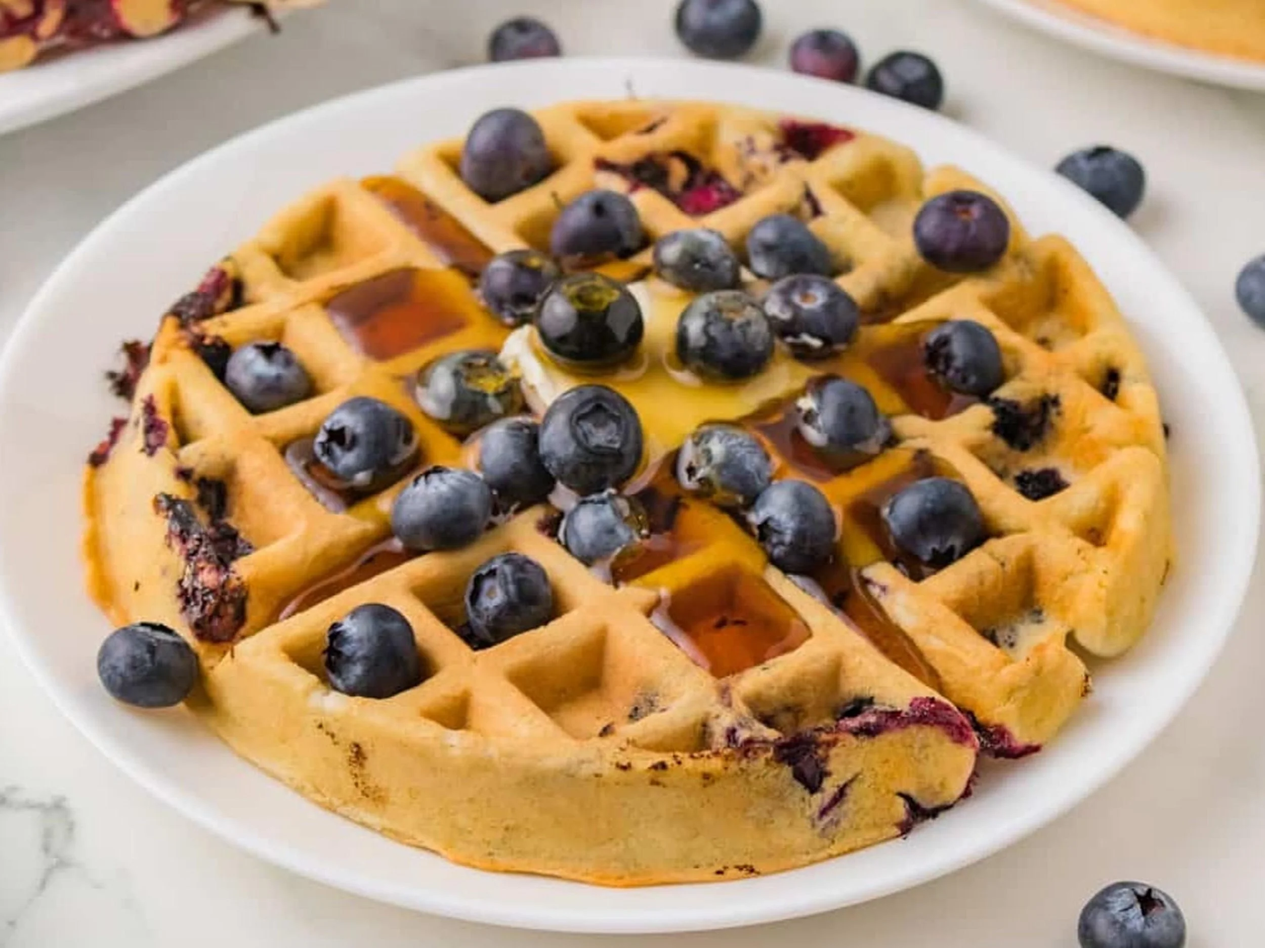 Waffle with blueberries and syrup on a white plate.