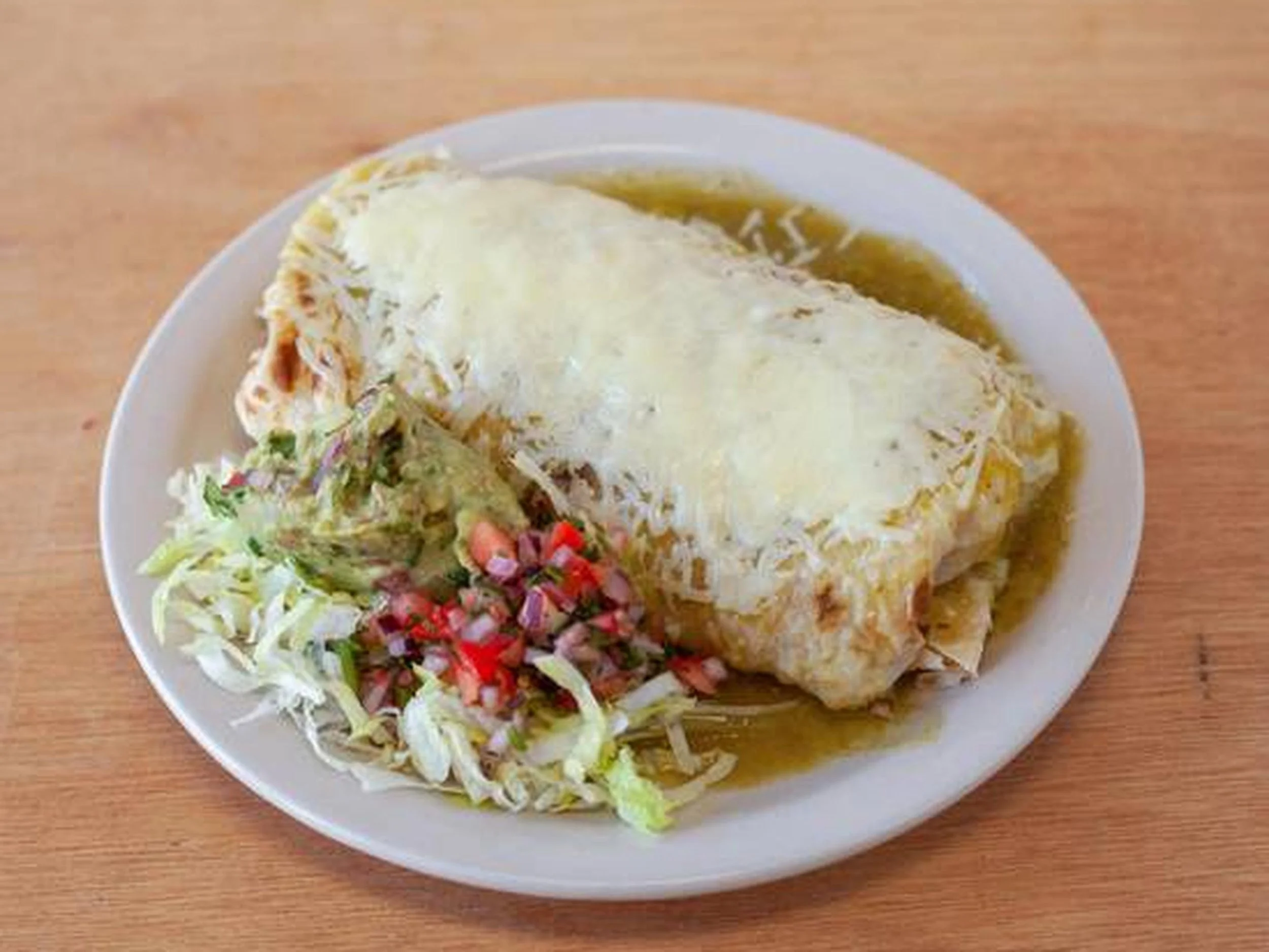 A plate of Mexican enchiladas topped with melted cheese, served with shredded lettuce and diced tomatoes.