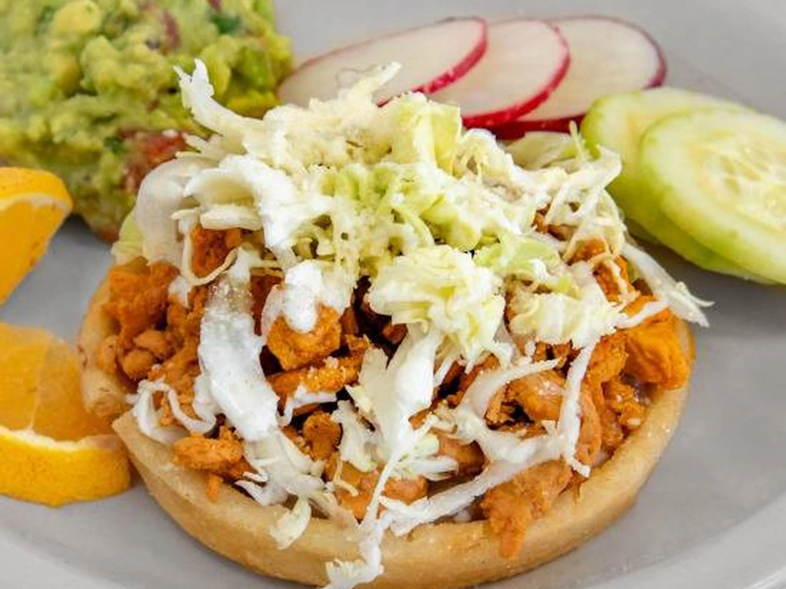 Fried fish fillet topped with shredded lettuce and mayonnaise, served in a bread roll, with lemon wedges and sliced radishes on the side.