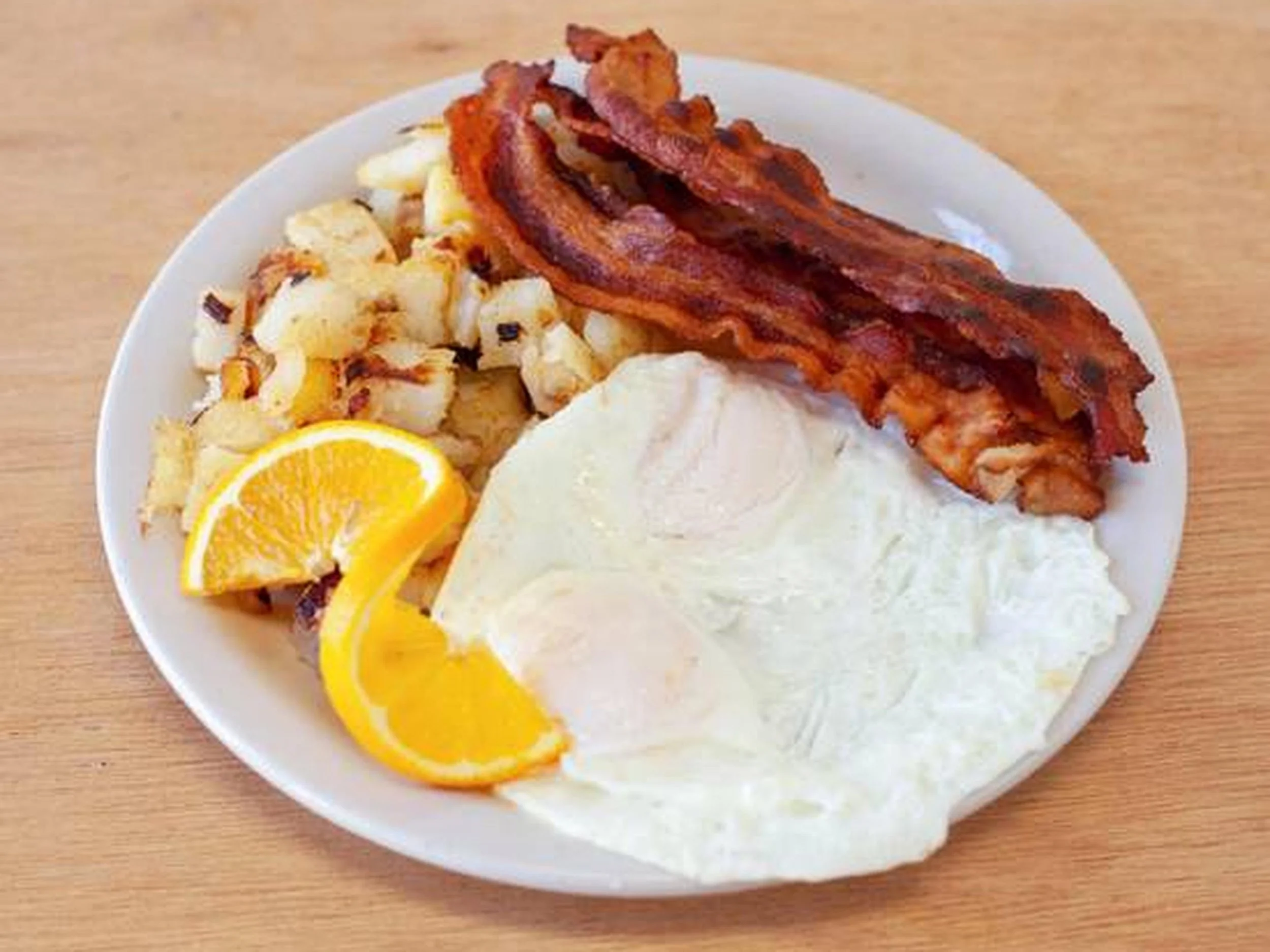 A white plate with bacon, scrambled eggs, lemon wedges, and a large serving of white gravy or cream.