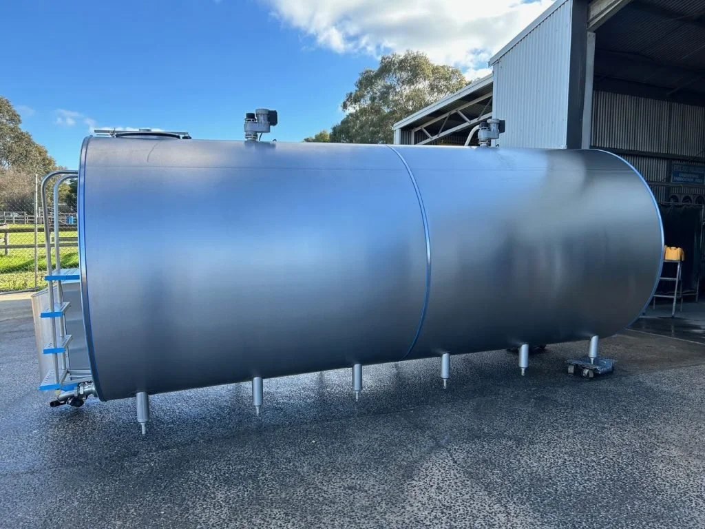 Large stainless steel industrial tank outside near a warehouse.