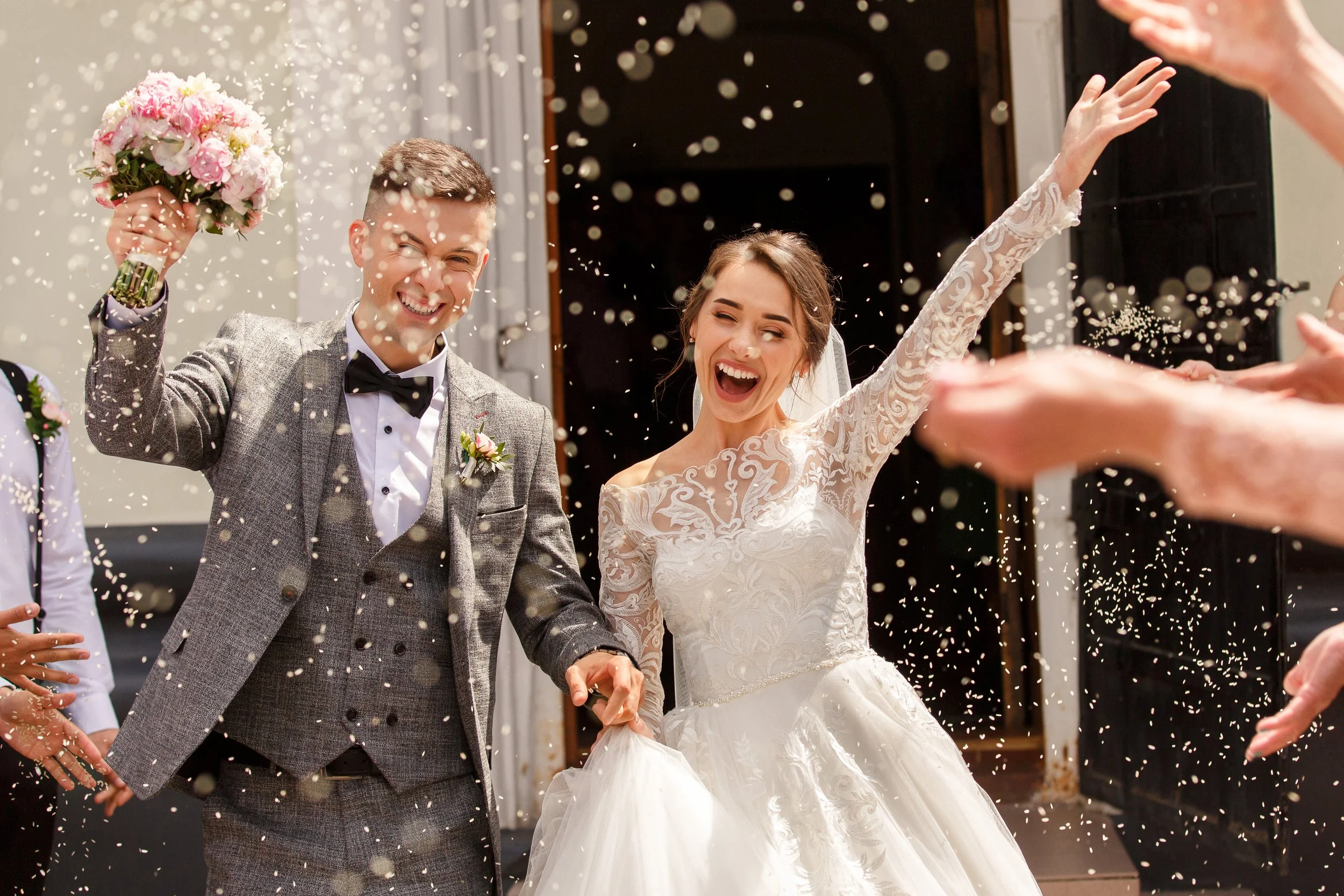 A happy bride and groom celebrating their wedding with guests throwing confetti in the air.