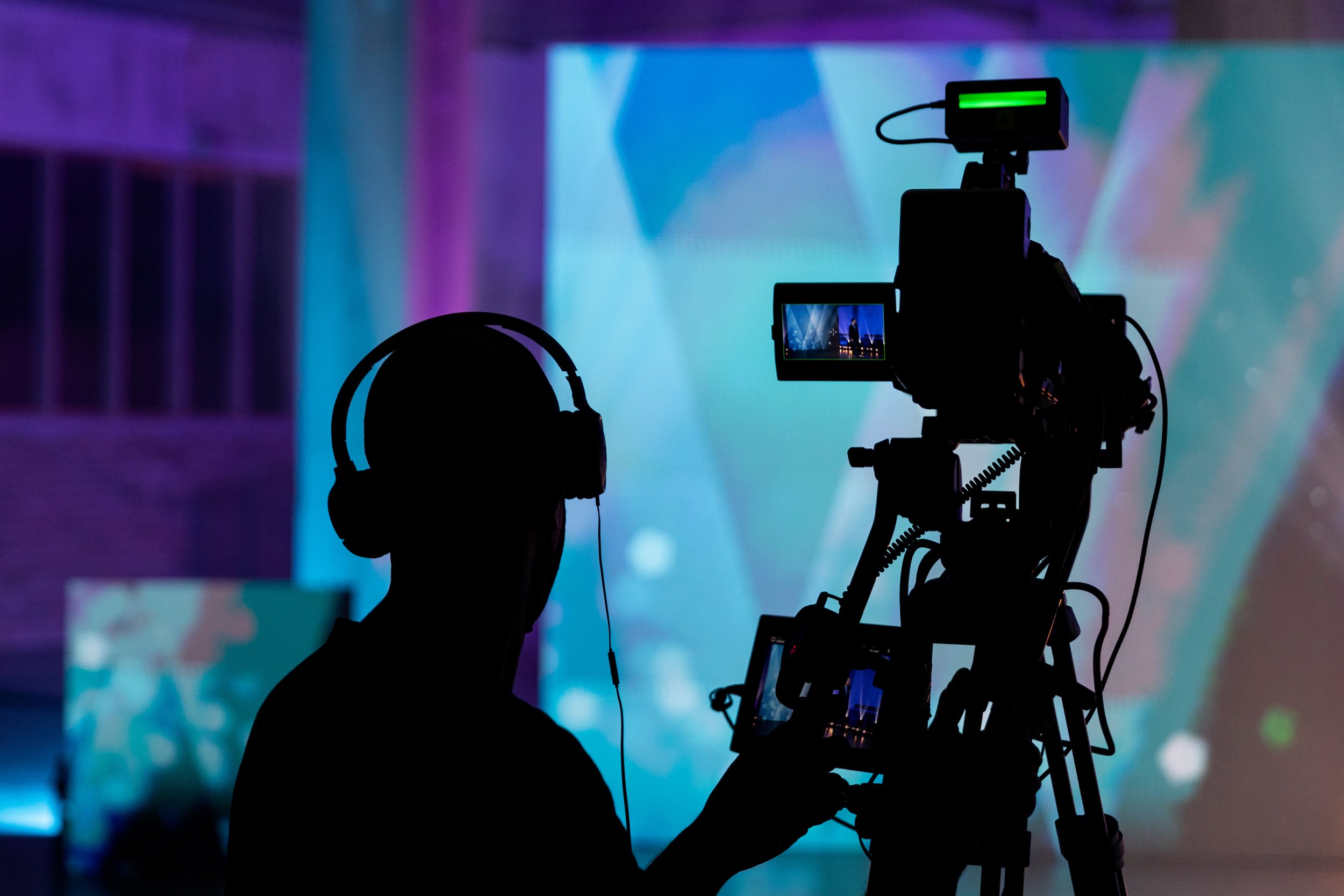 A silhouette of a person operating a professional video camera or filming equipment against a colorful, abstract background.