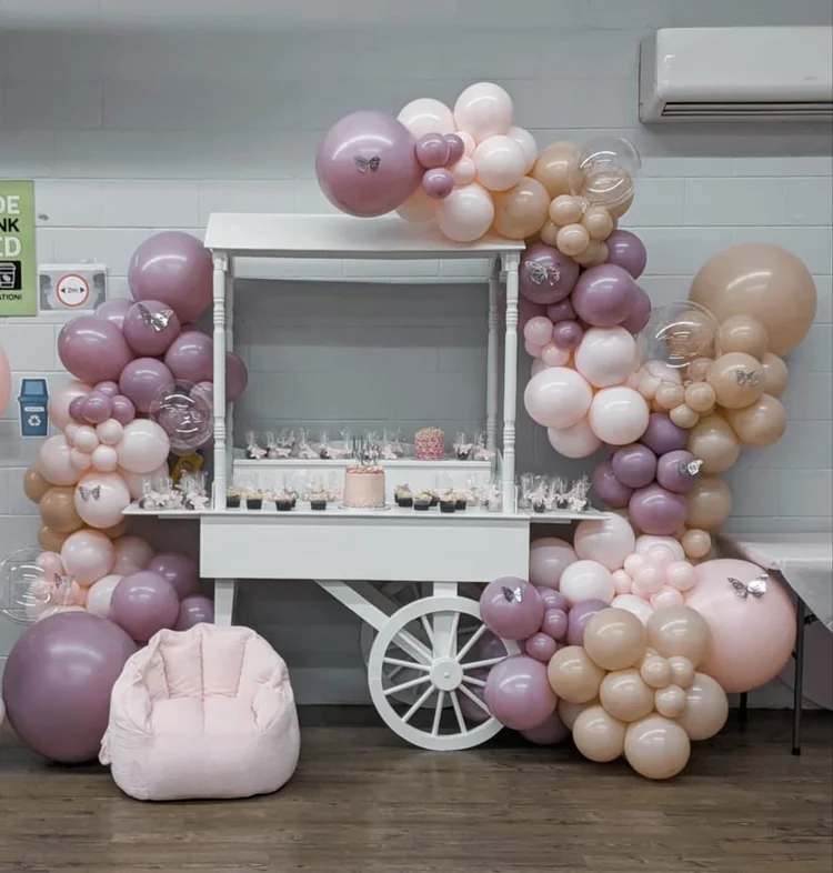 White sweet cart framed by a mauve and blush balloon arch