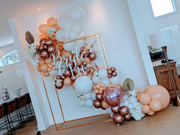 Gold metal frame with rose gold and peach balloon garland and wooden sign