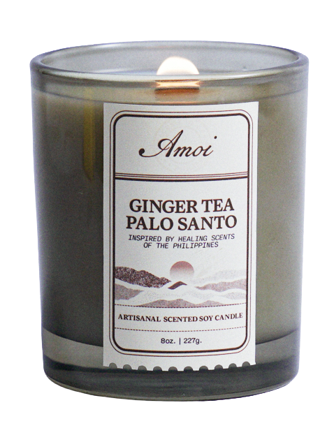 A lit scented soy candle labeled 'Amoi Ginger Tea Palo Santo' in a glass container