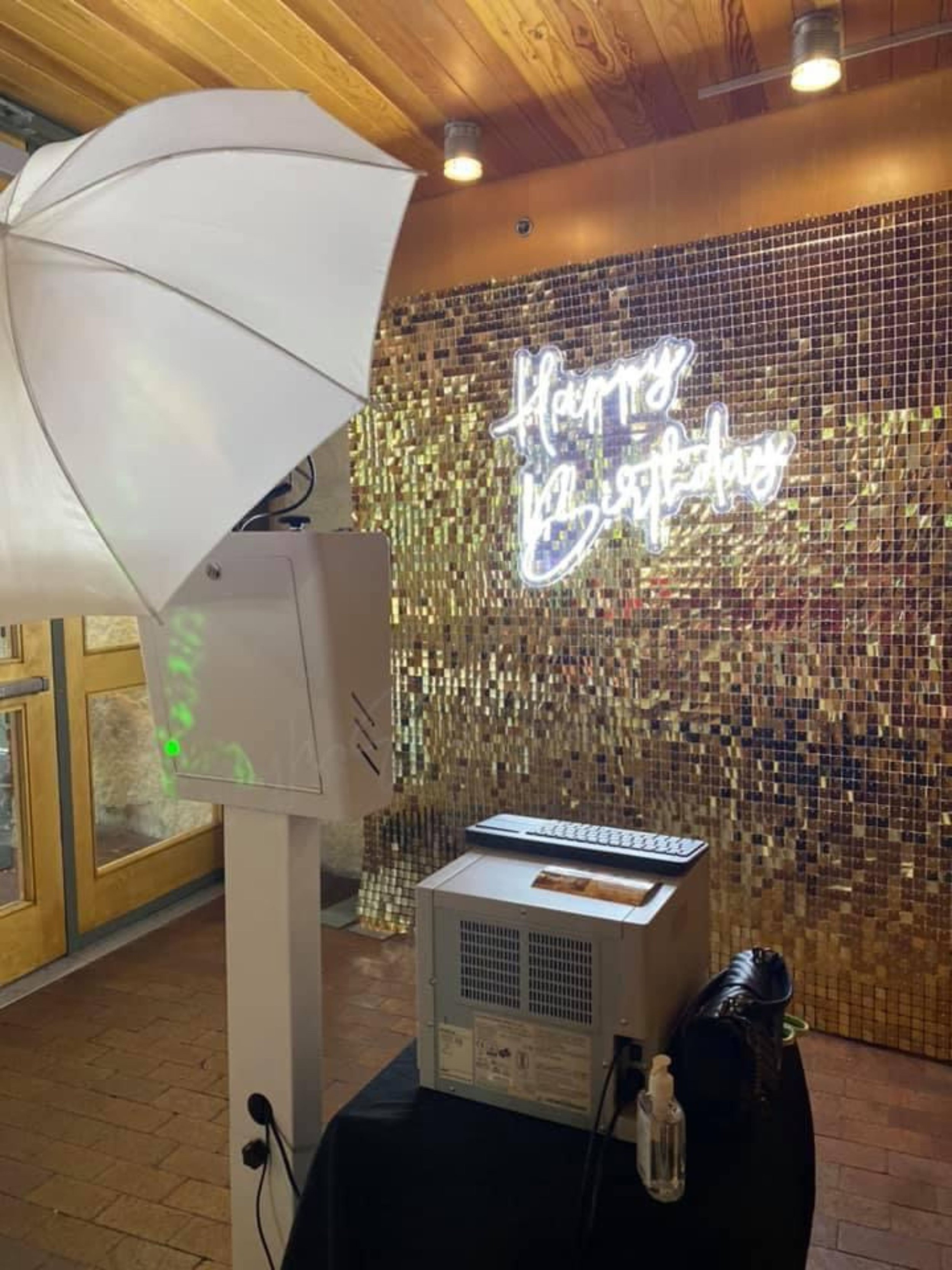 A photo of a digital check-in kiosk near a wooden door, with a large umbrella for shade, situated in a warm-toned indoor setting with wood-paneled walls and a golden mosaic backdrop.