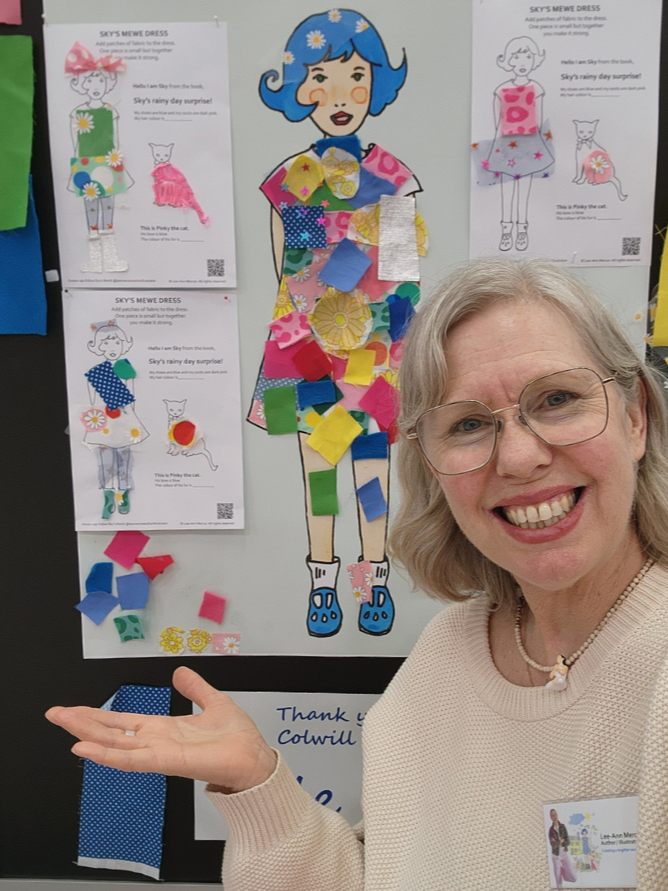 A smiling woman with glasses and blonde hair stands next to a colorful dress-up poster. The poster features a cartoon girl with blue hair and a patchwork dress decorated with fabric swatches. The woman gestures towards the poster with her left hand, and there are fabric pieces attached to the poster and some scattered at the bottom.