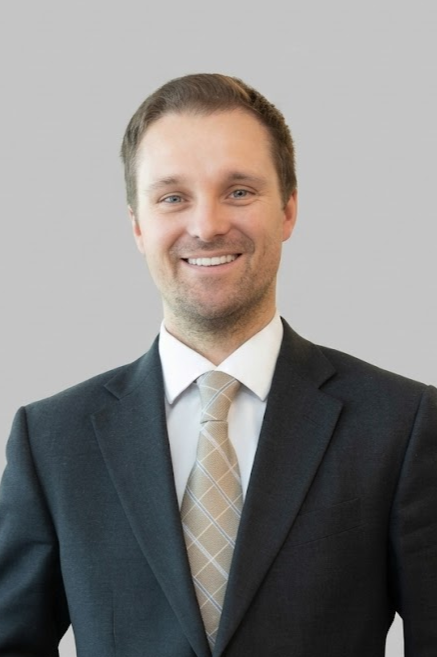 Portrait of a man in a suit and tie smiling against a neutral background.