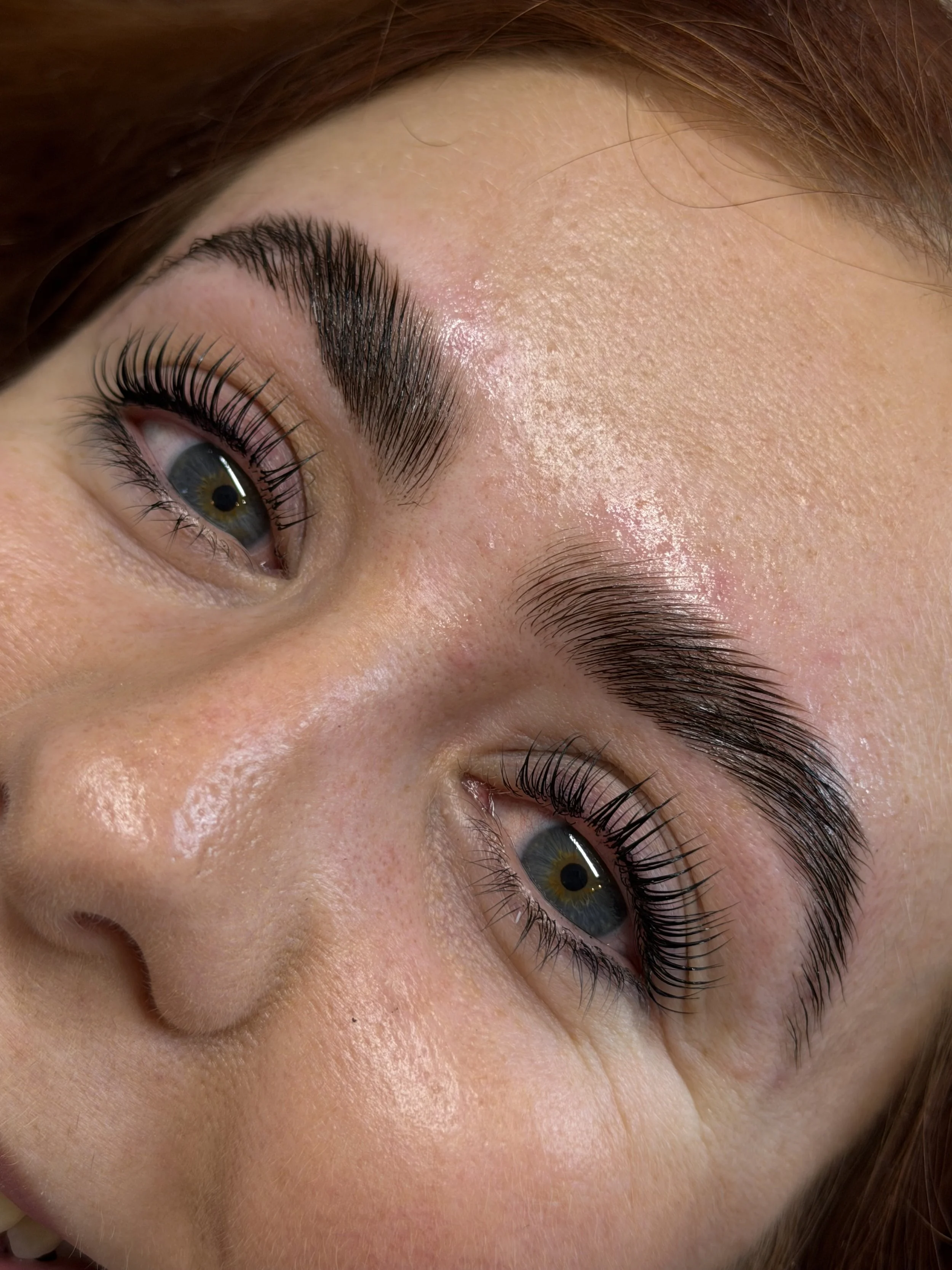 Close-up of a person's eye with makeup, including long eyelashes, groomed eyebrows, and visible skin texture.