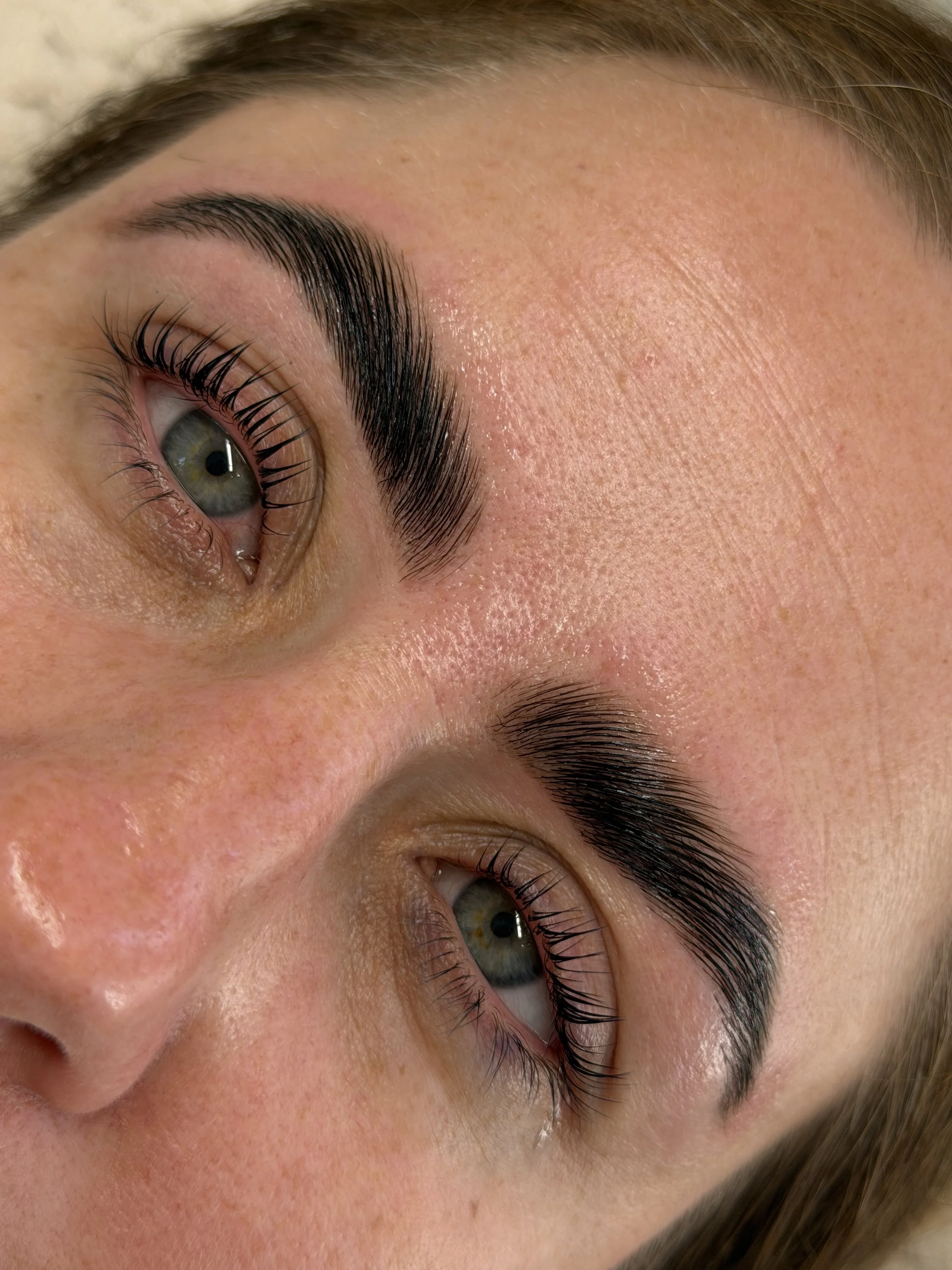 Close-up of a person's eye with groomed eyebrows and long eyelashes, showing detailed skin texture.