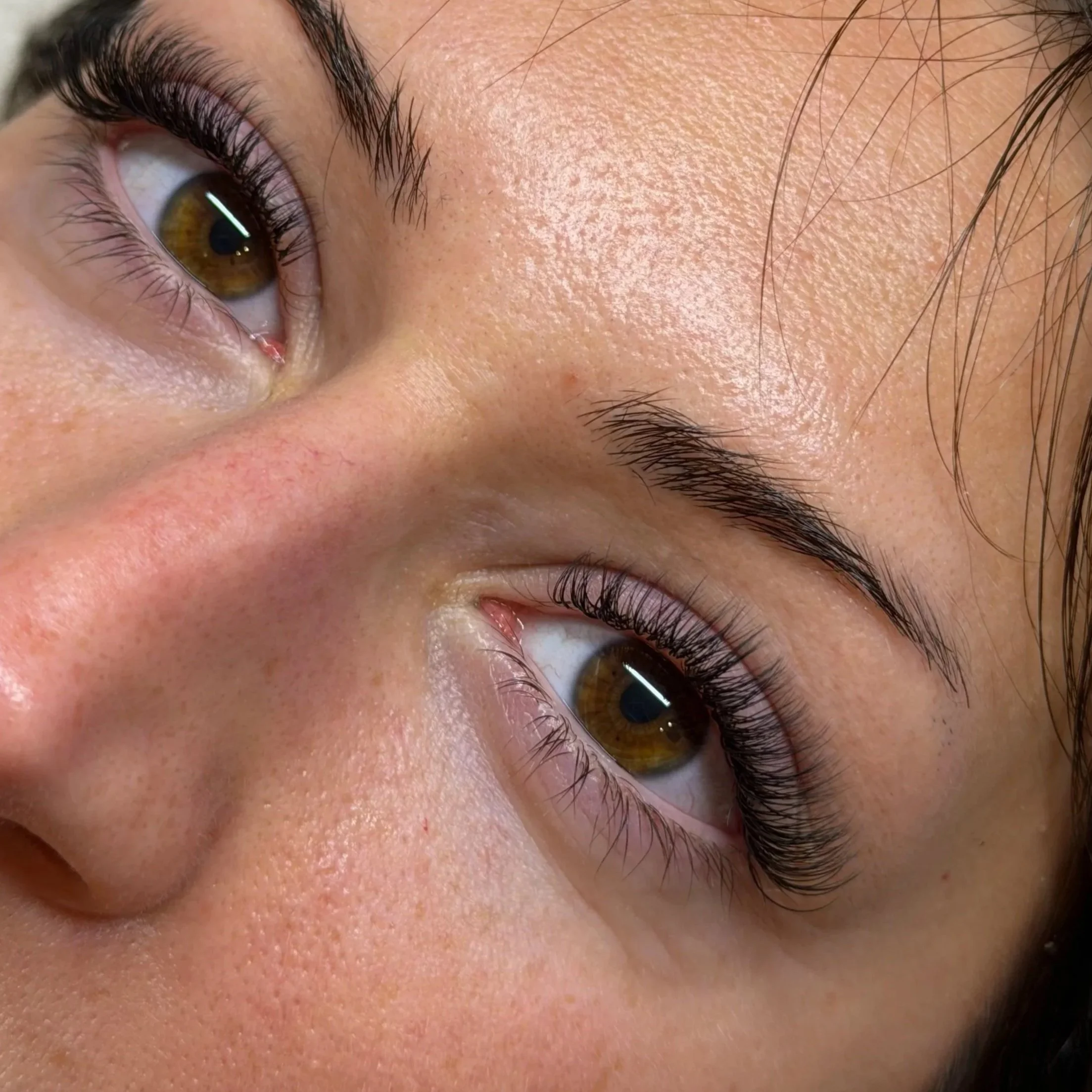 Close-up of a person's eye showing brown iris, long eyelashes, and eyebrow, with skin and some facial hair visible.