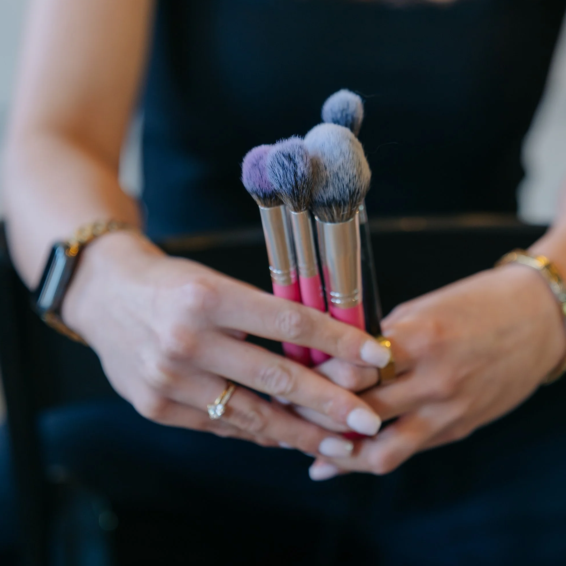Close-up of a person's hand holding a set of makeup brushes with fluffy bristles.