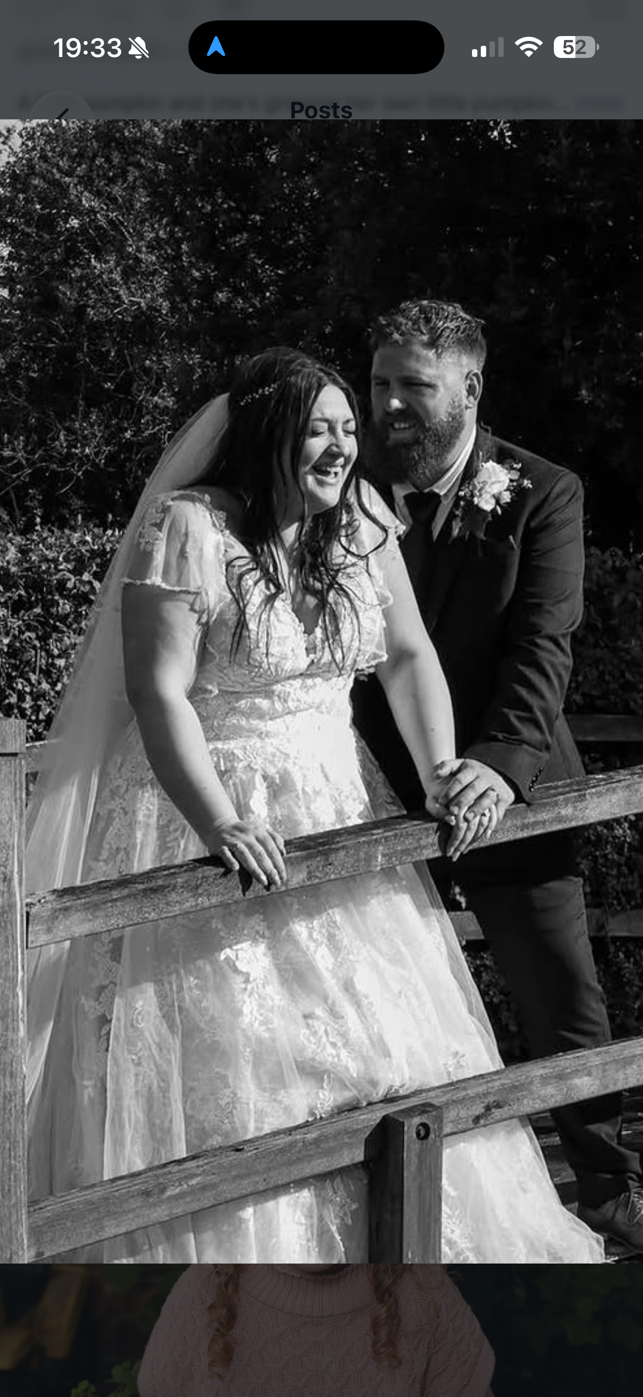 Black and white photo of a bride and groom on their wedding day, laughing and holding hands over a wooden fence outdoors.