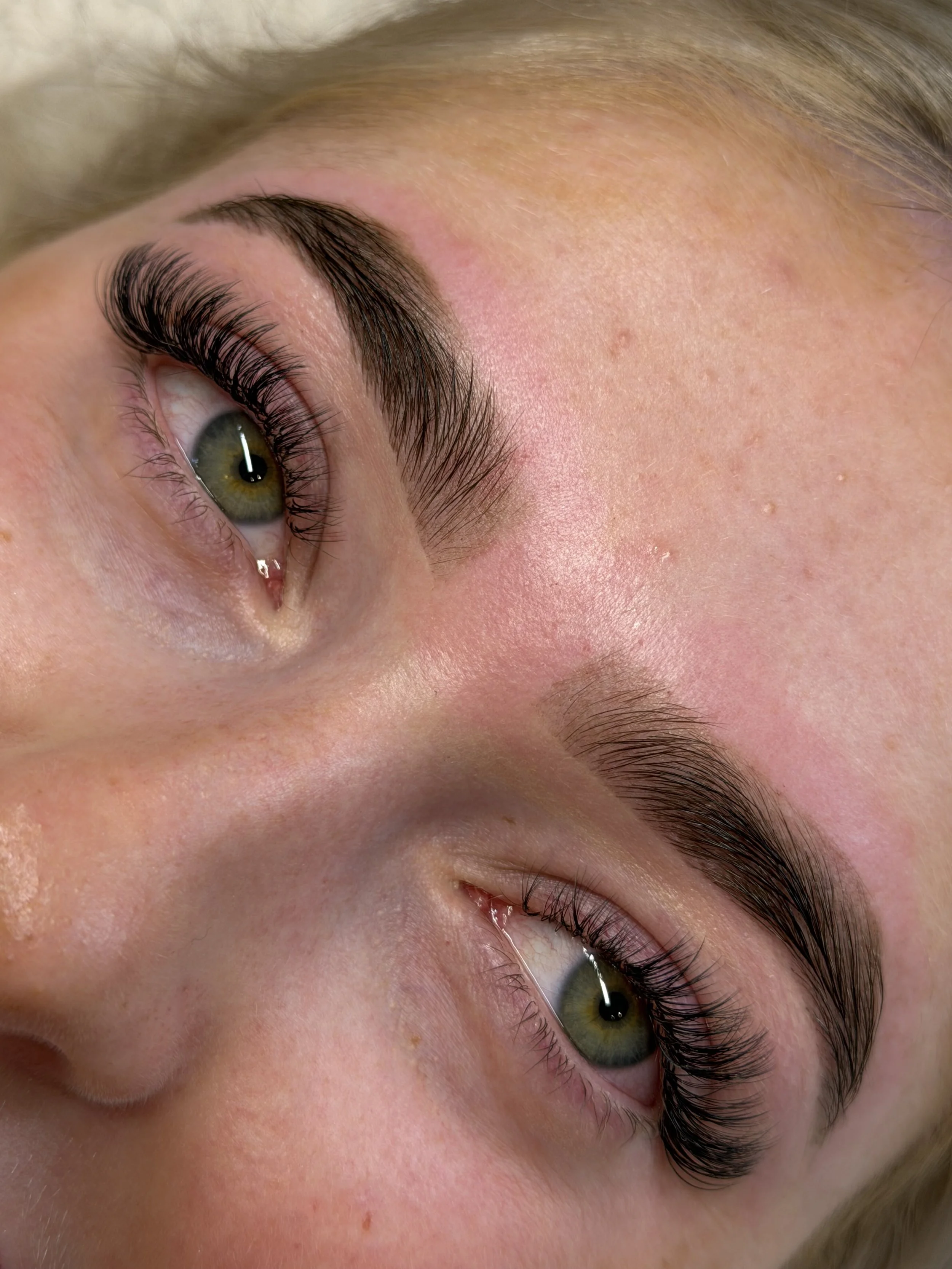 Close-up of a person's eye with long eyelashes, and the skin around the eye showing some freckles and redness.
