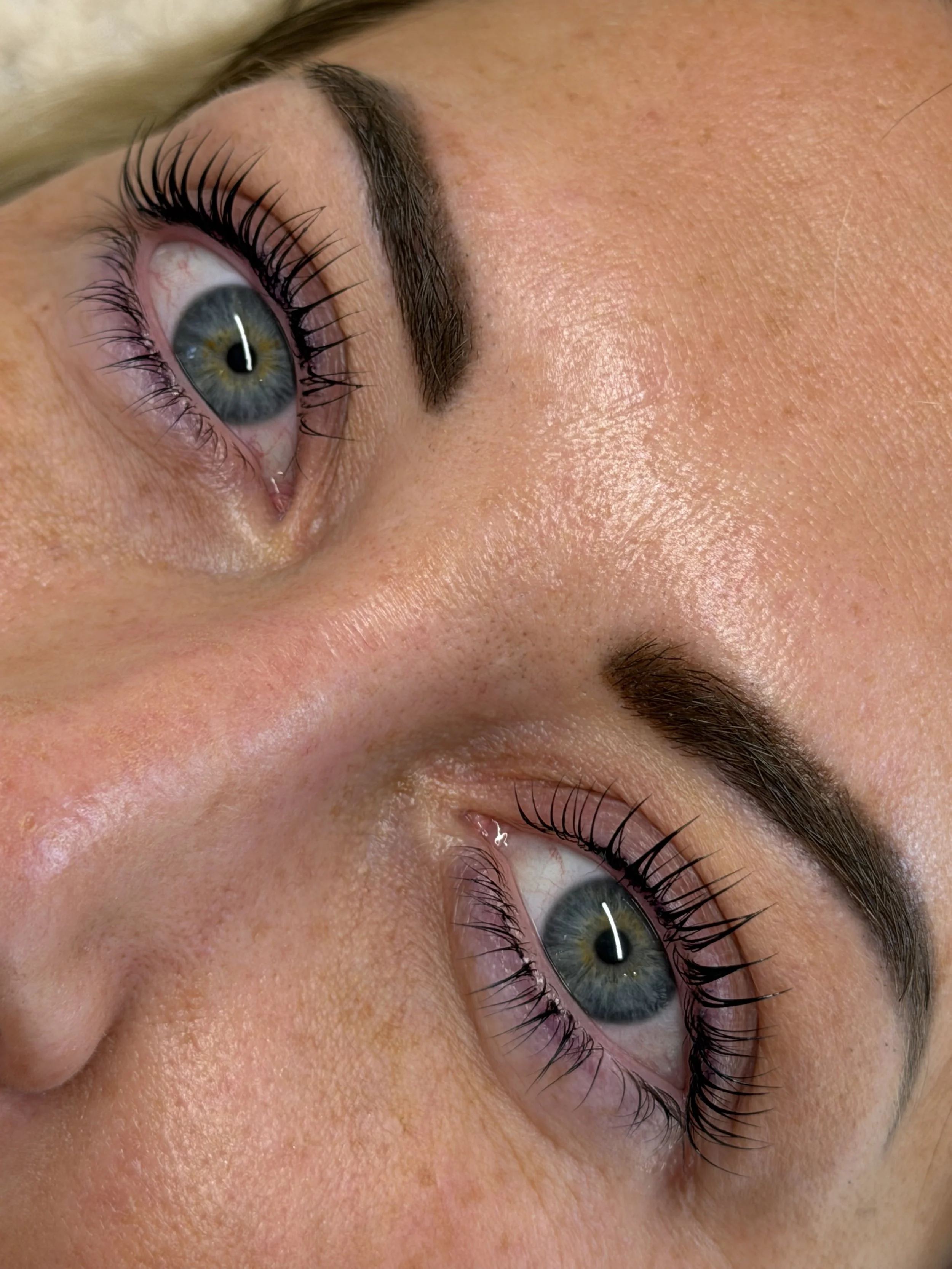 Close-up of a woman with blue eyes, long eyelashes, and well-groomed eyebrows, showing a partial view of her face.