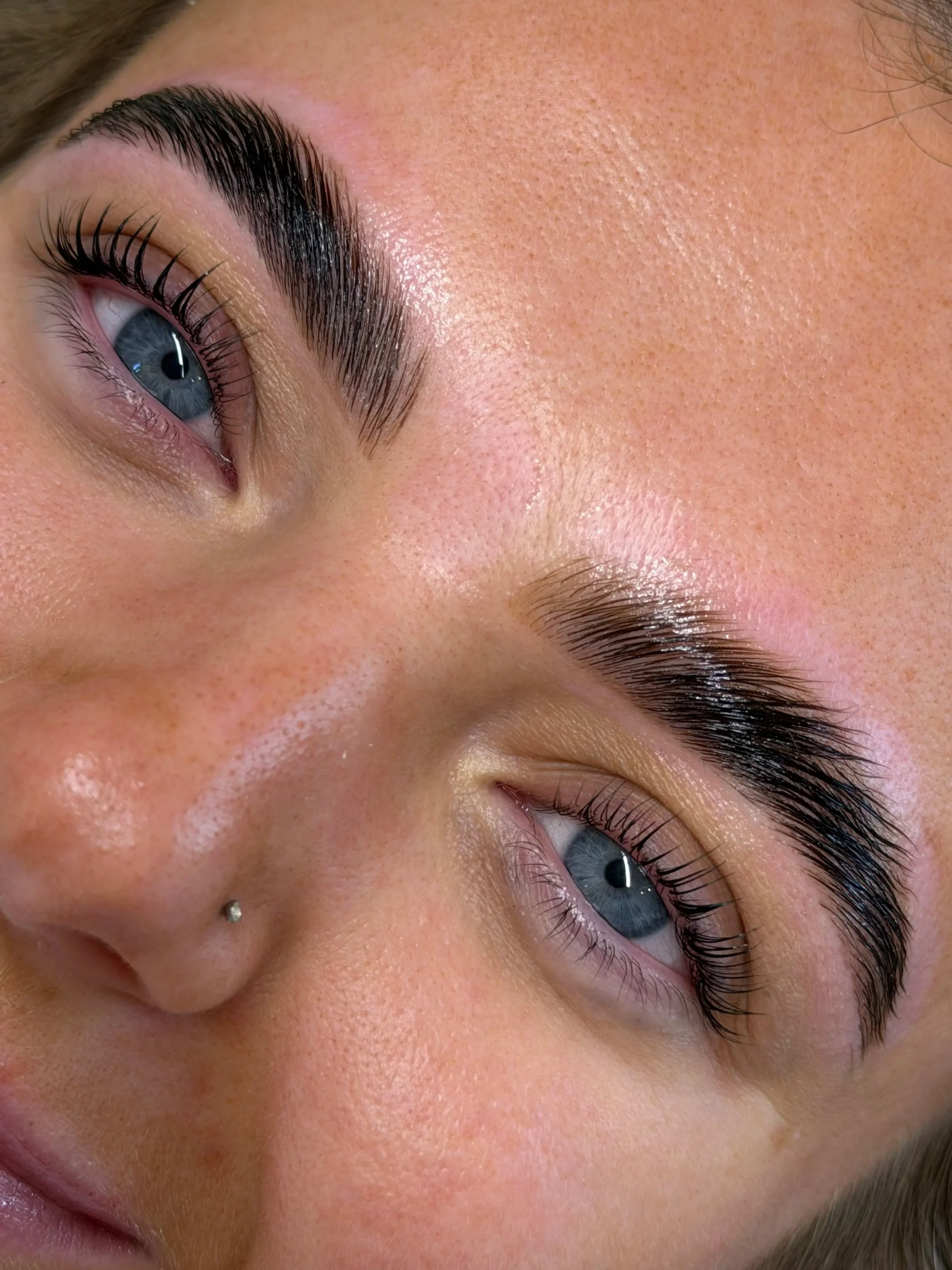 Close-up image of a person with bright blue eyes, well-groomed eyebrows, and clear skin, lying down with eyes open.