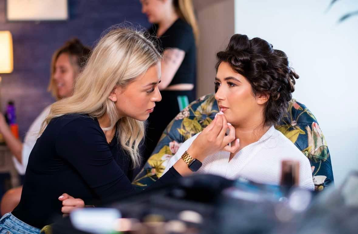 Makeup artist applying makeup to a woman seated in a chair during a beauty or makeup session in a salon or studio.